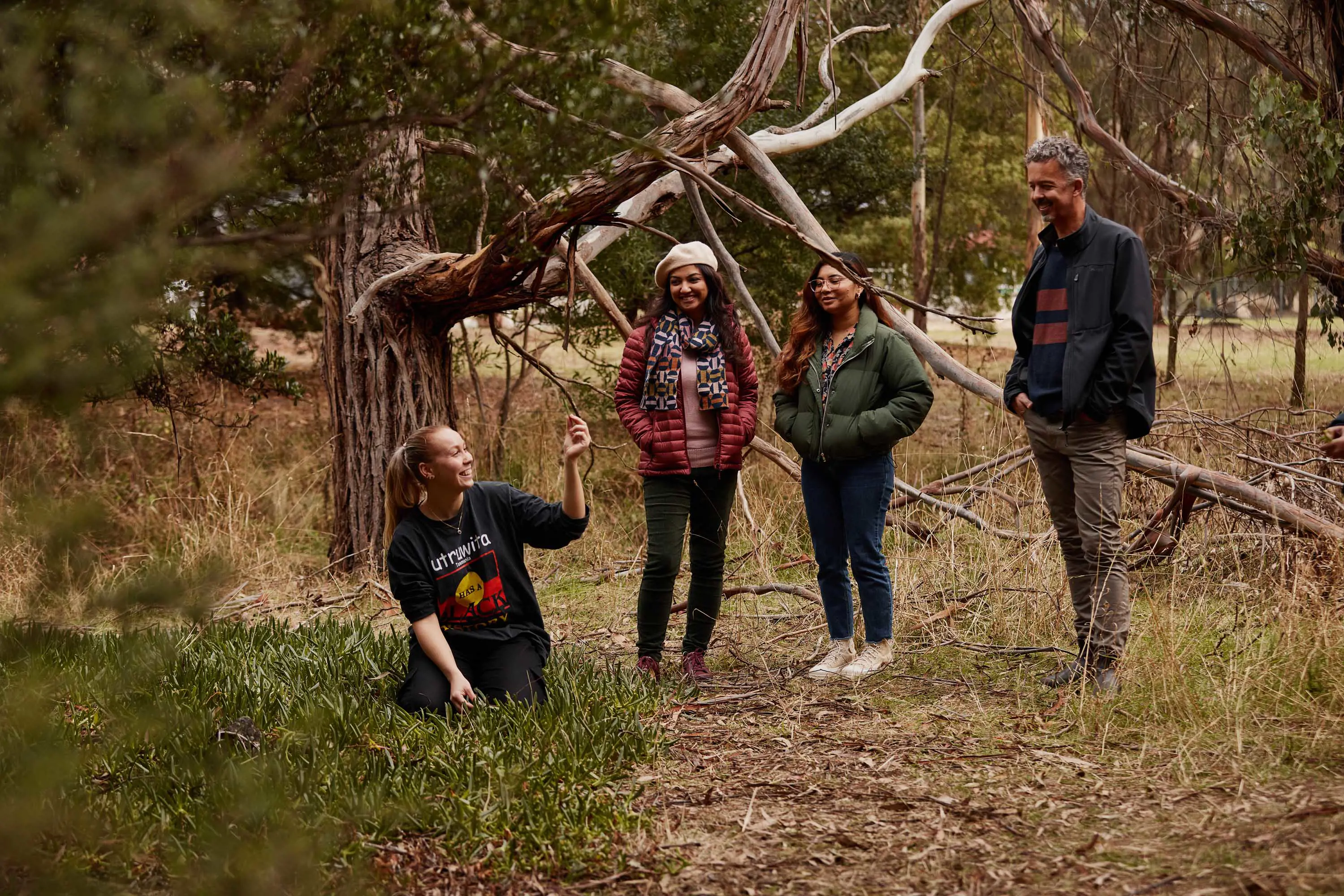 A small group stand with a guide who is picking wild plants from a path. 