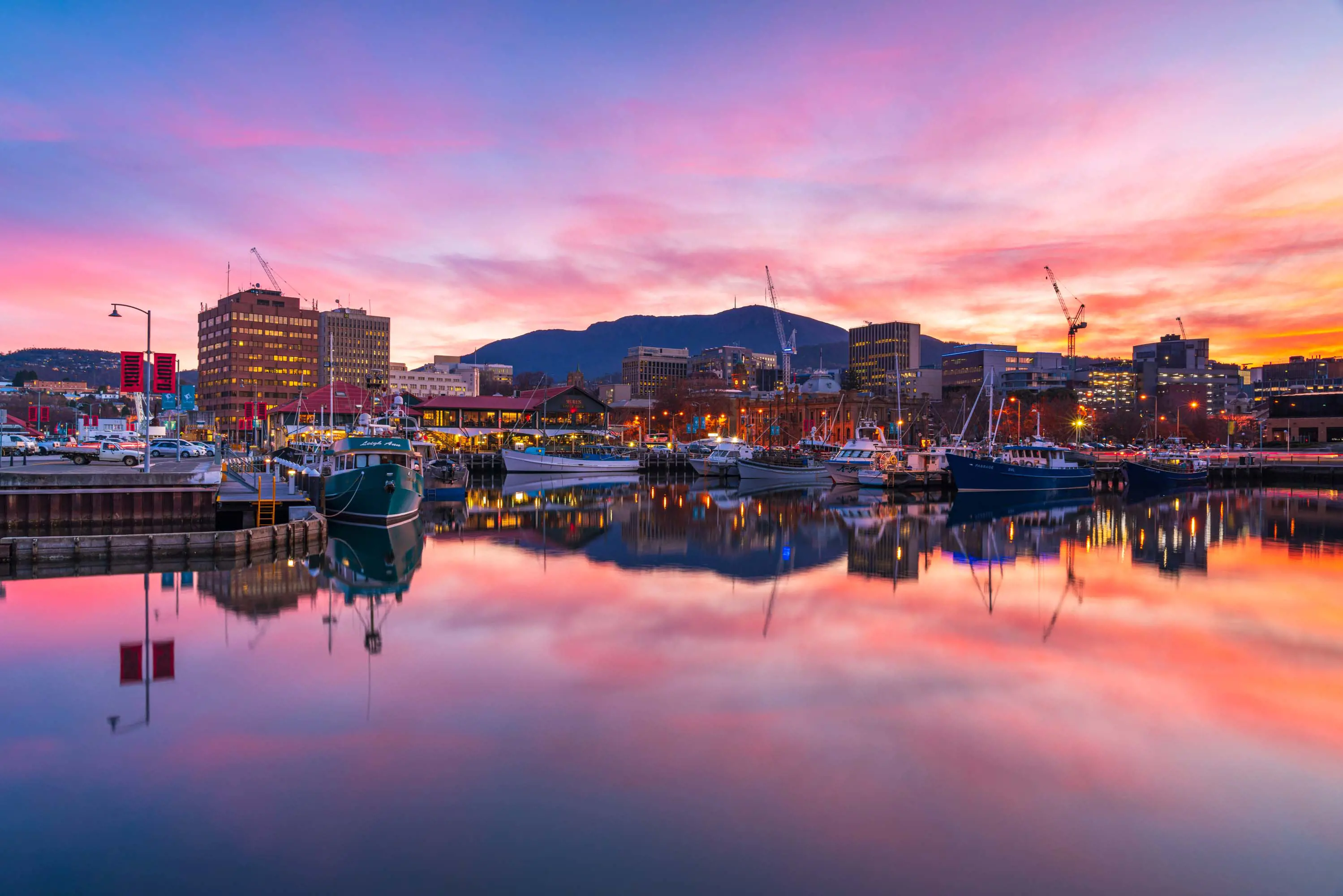 The Hobart cityscape is reflected perfectly into the water at the port during a brilliant pink and purple sunset.