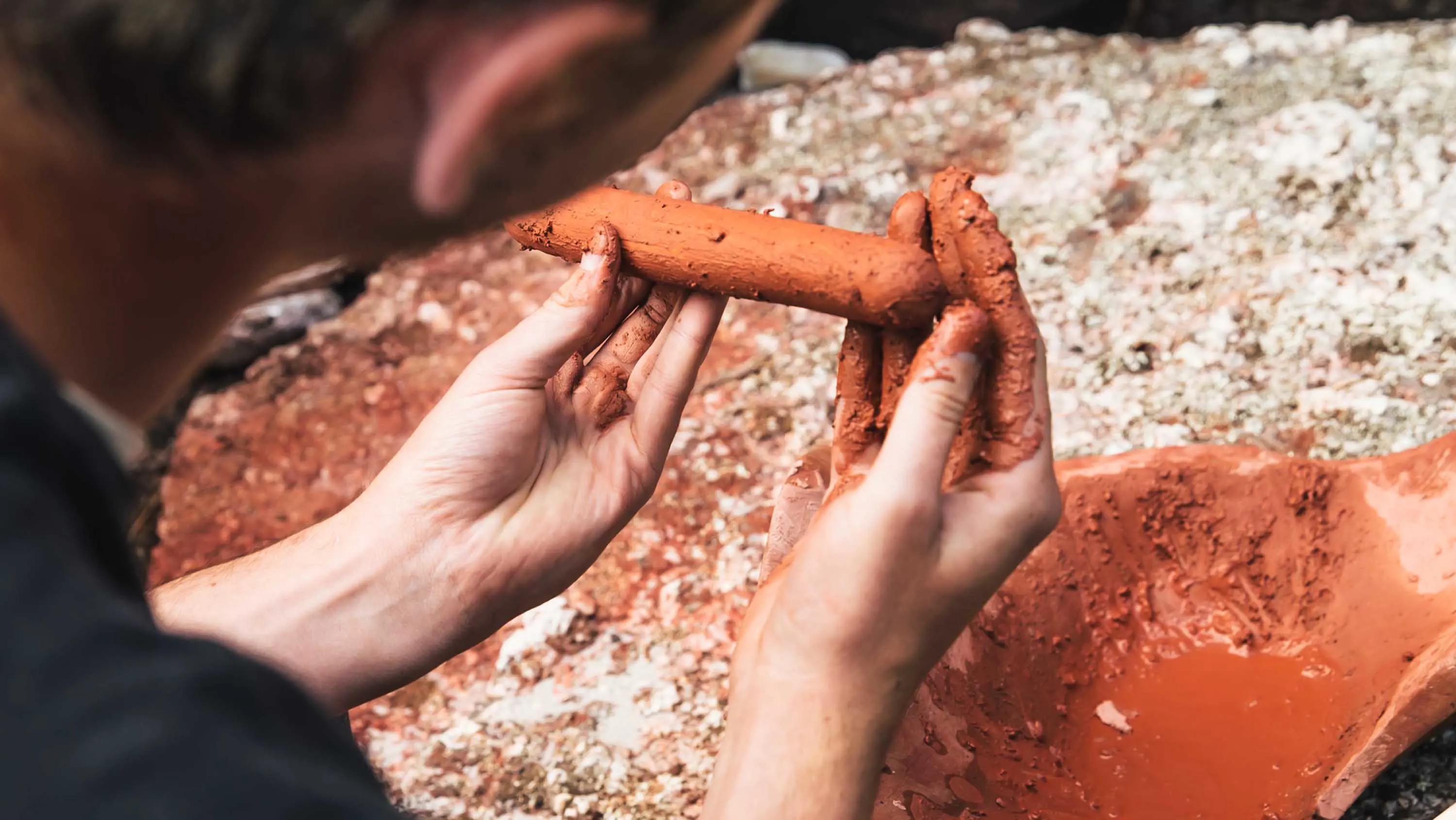 A man shapes red-coloured clay.