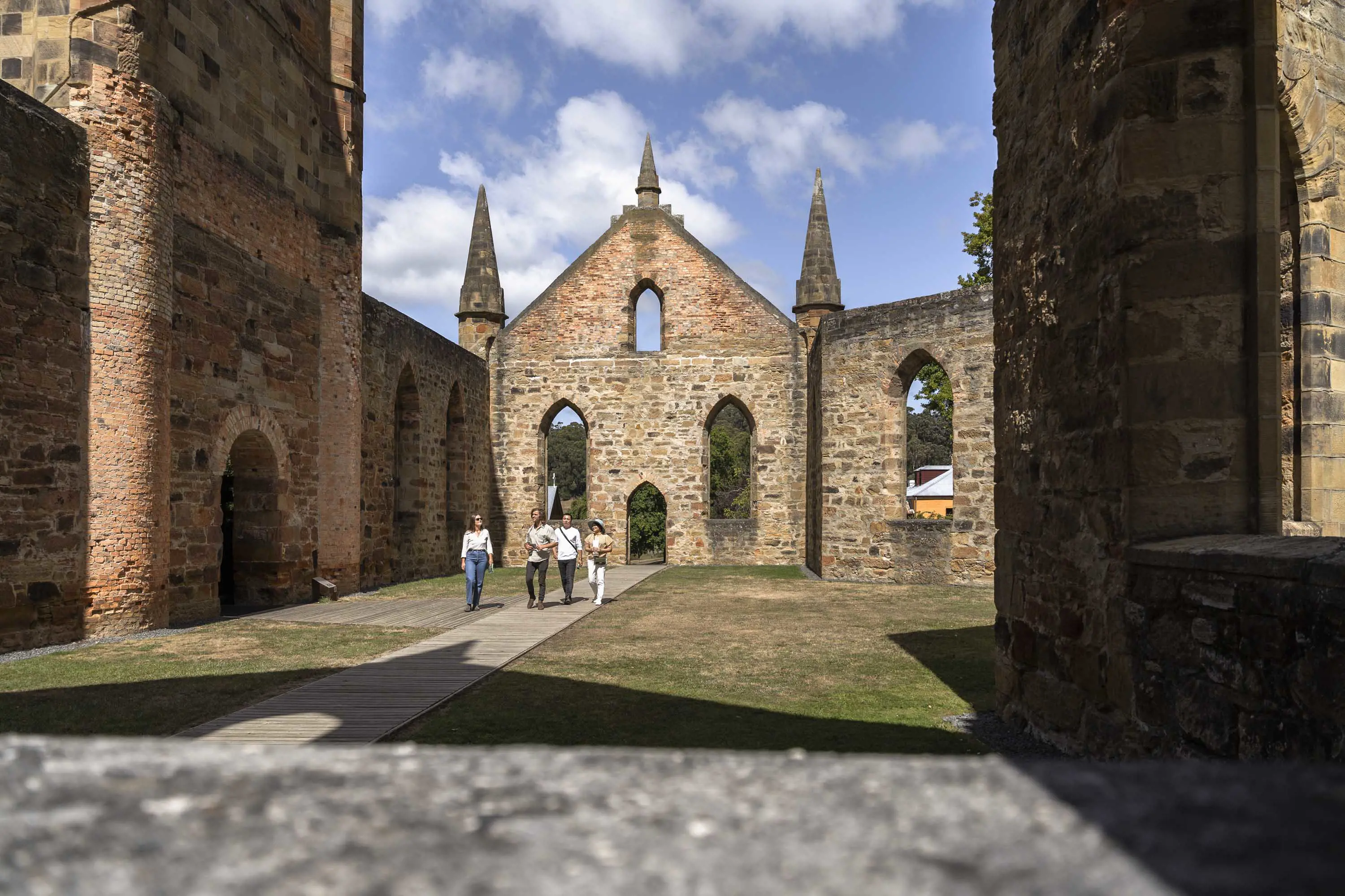 A small group of young people walk through the well-preserved ruins of an old church, made from red brick and sandstone.