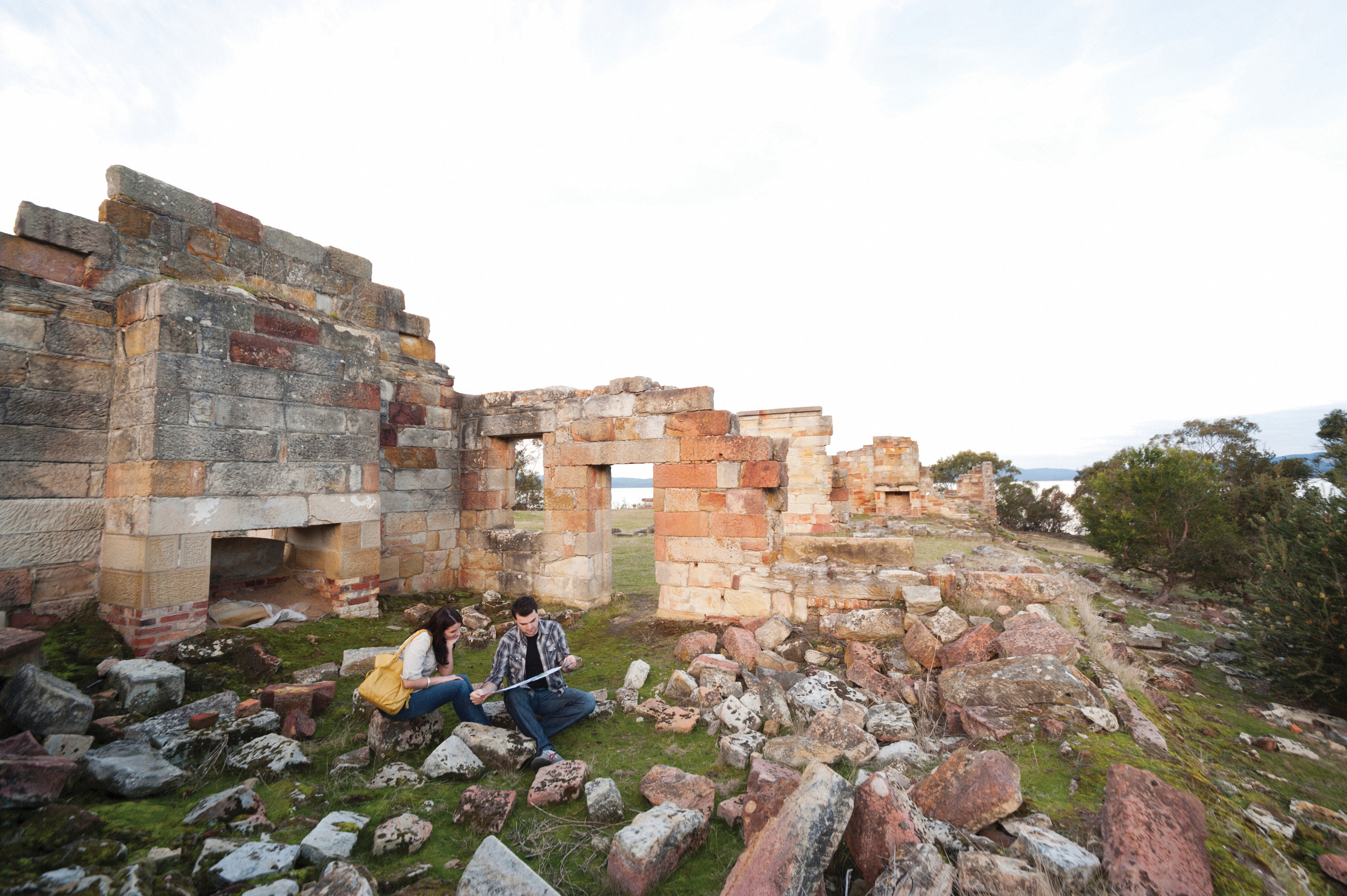 A man and woman sat on rocks looking at the Coal Mines Historic Site situated on the Turrakana / Tasman Peninsula.