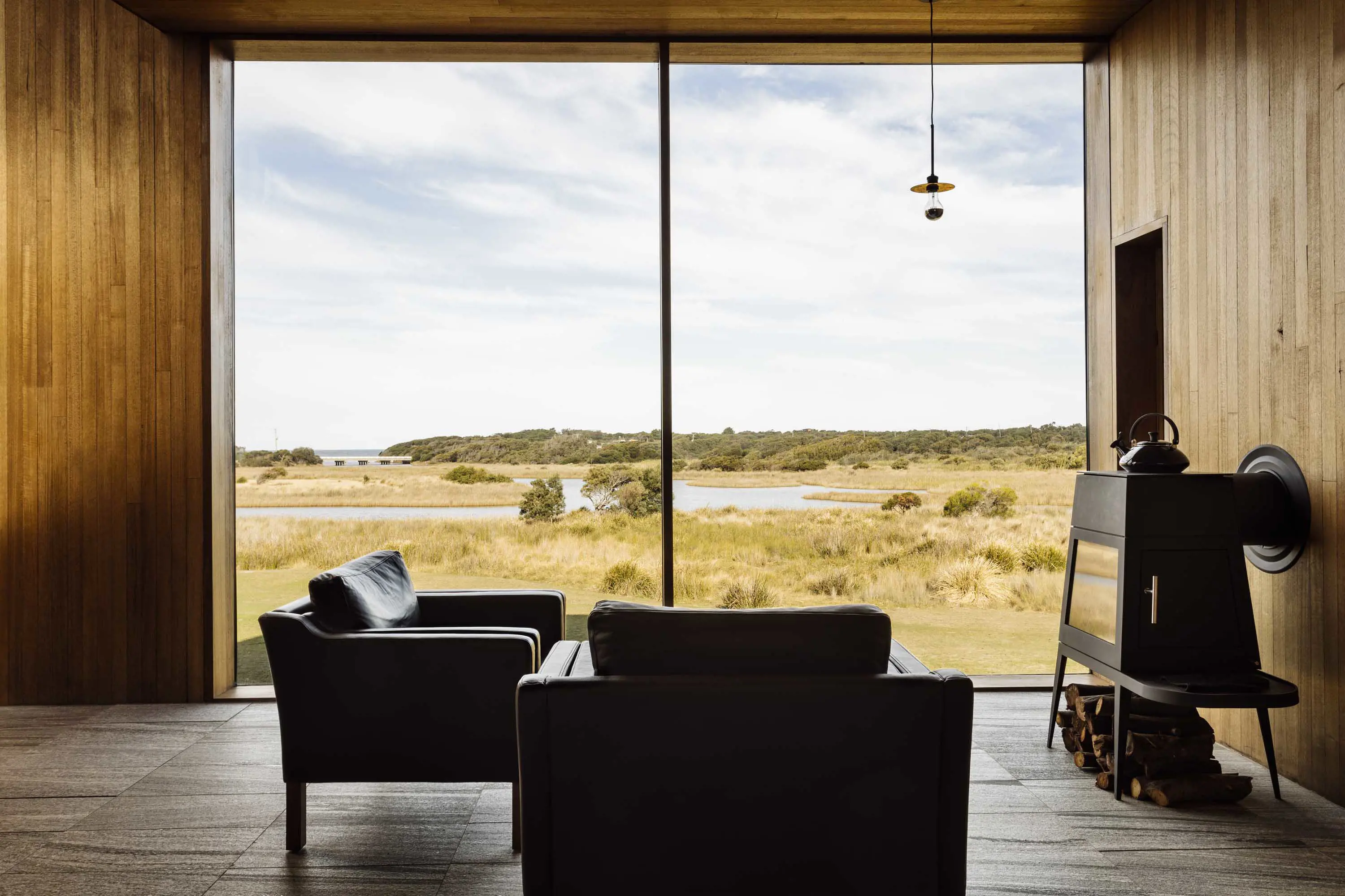 A modern interior with minimalist furniture looking out over grassland through a large floor to ceiling window.