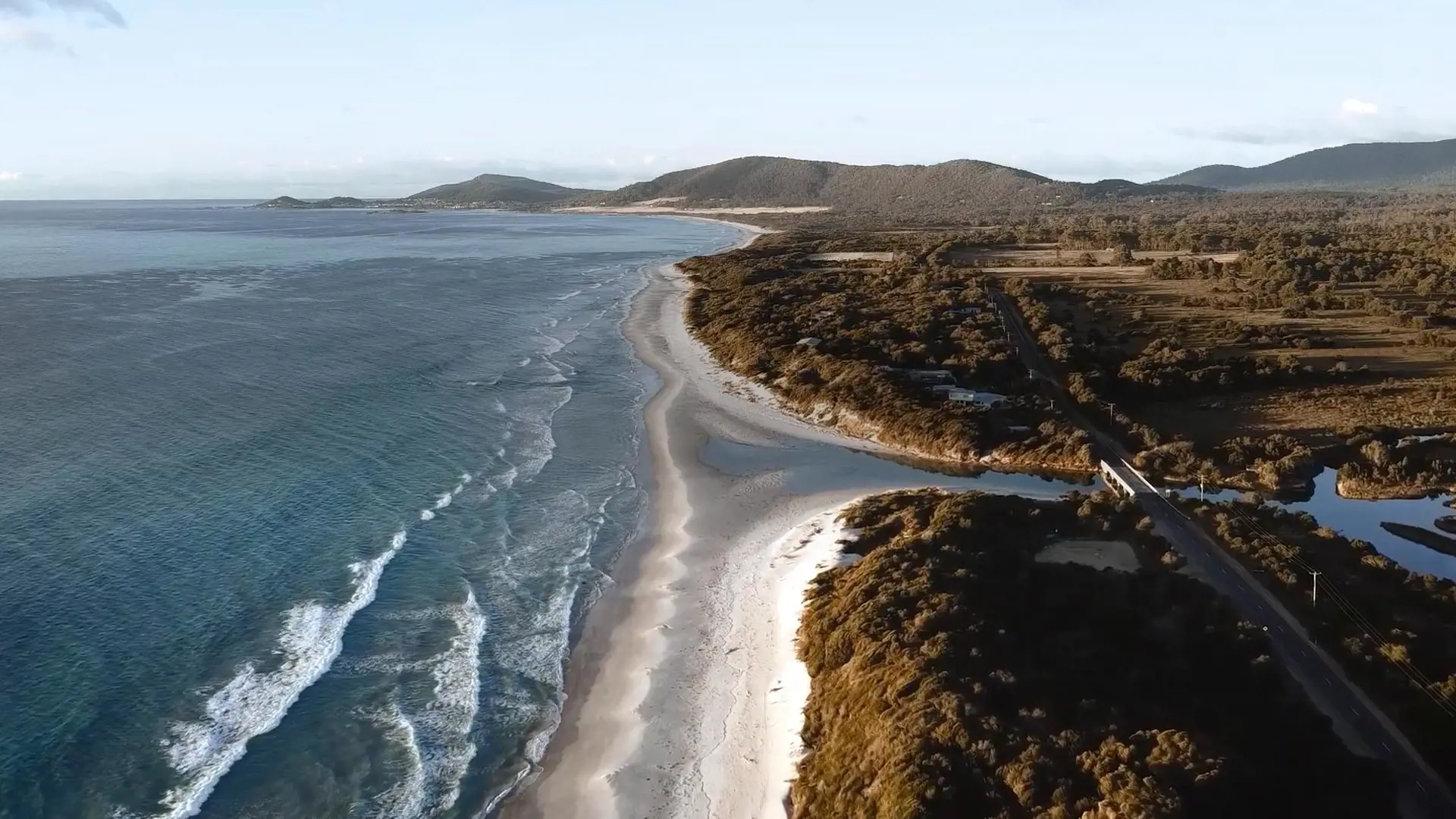 White beaches and blue water next to coastal bushland on a sunny day.