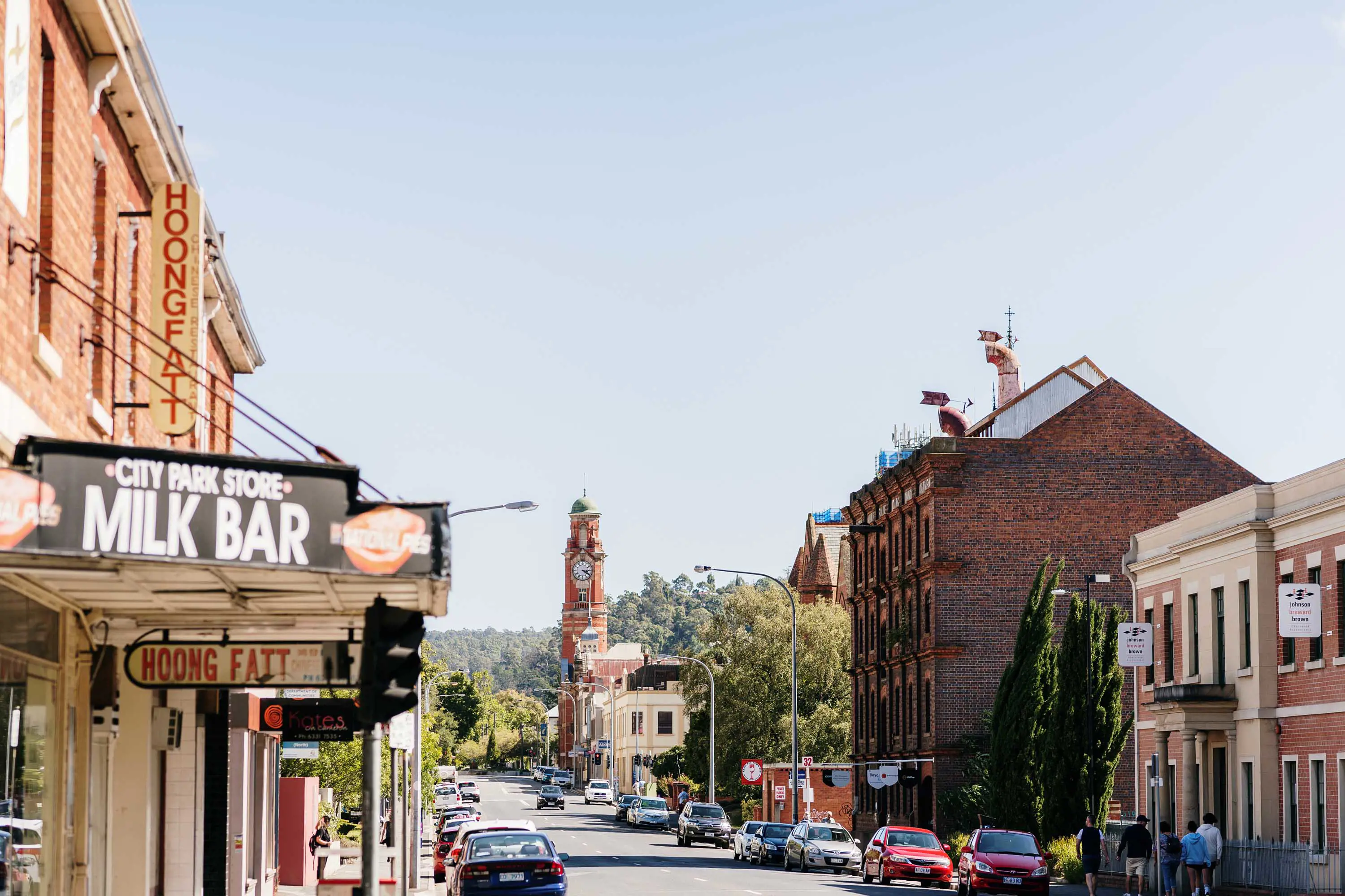 A wide, city street lined with old, two-storey brick buildings. One building has a sign that reads City Park Store Milk Bar.