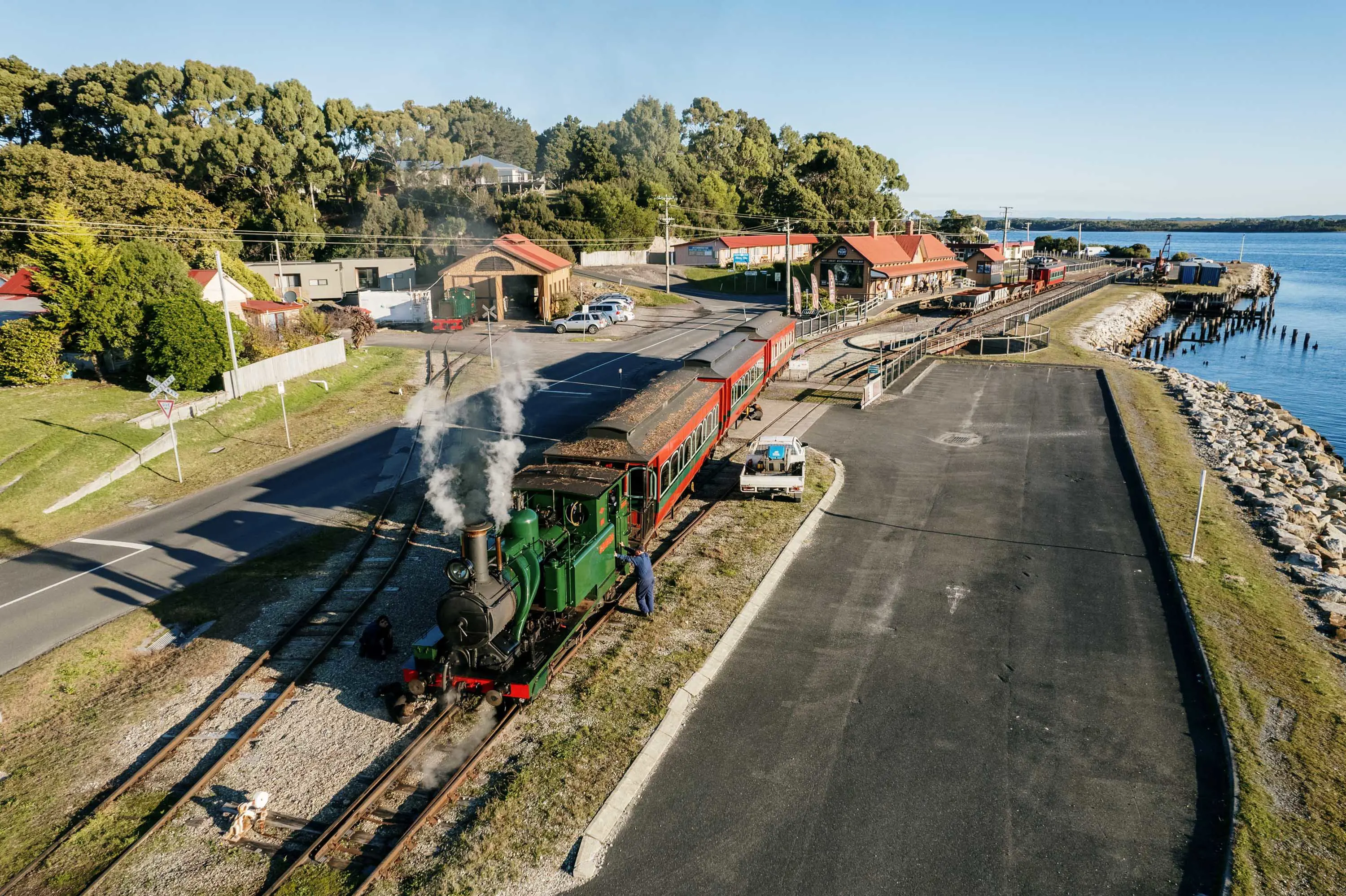 An aerial photograph of a green steam engine on a railway line next to a river.