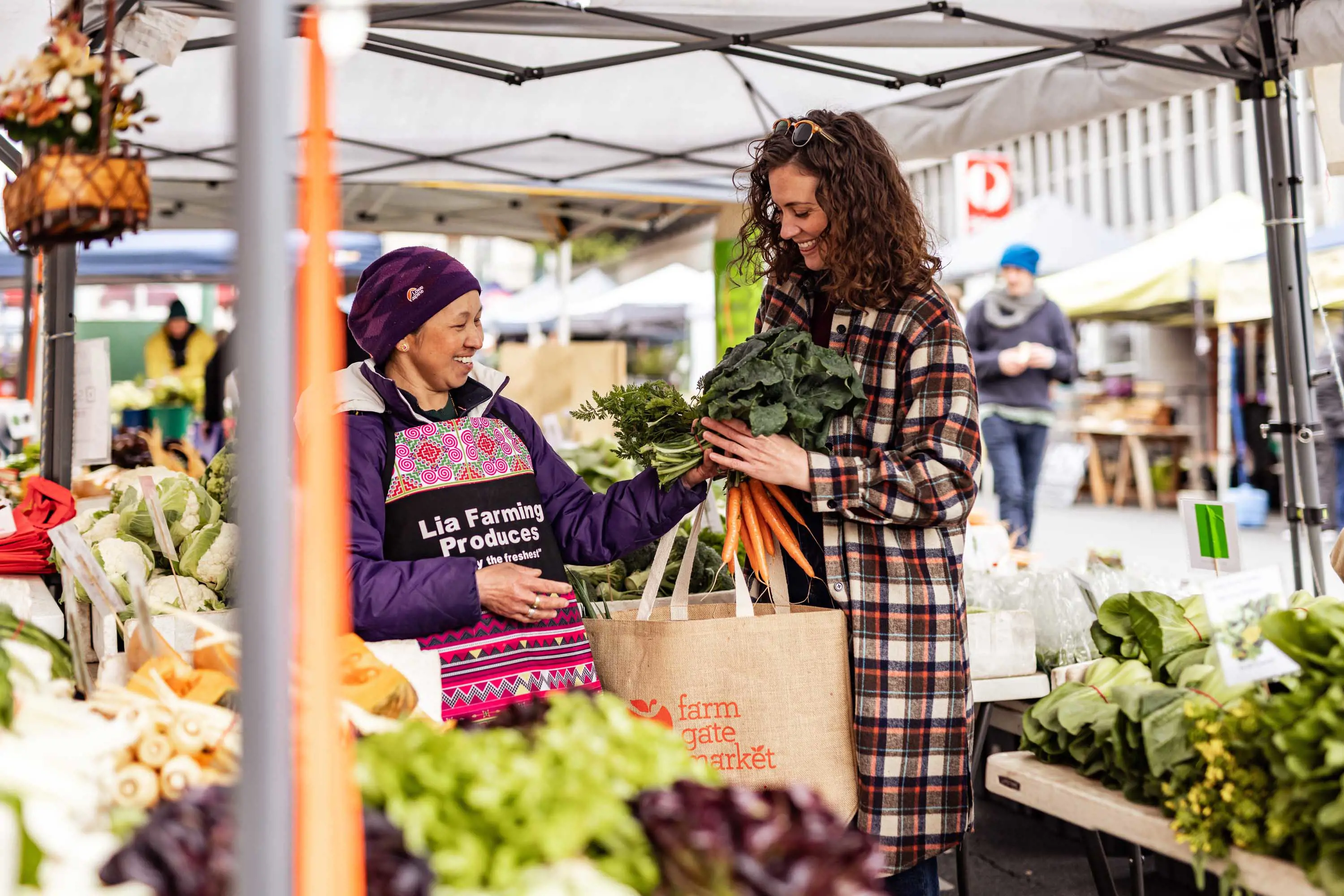 A woman is a winter coat talks with the owner of a vegetable stall.