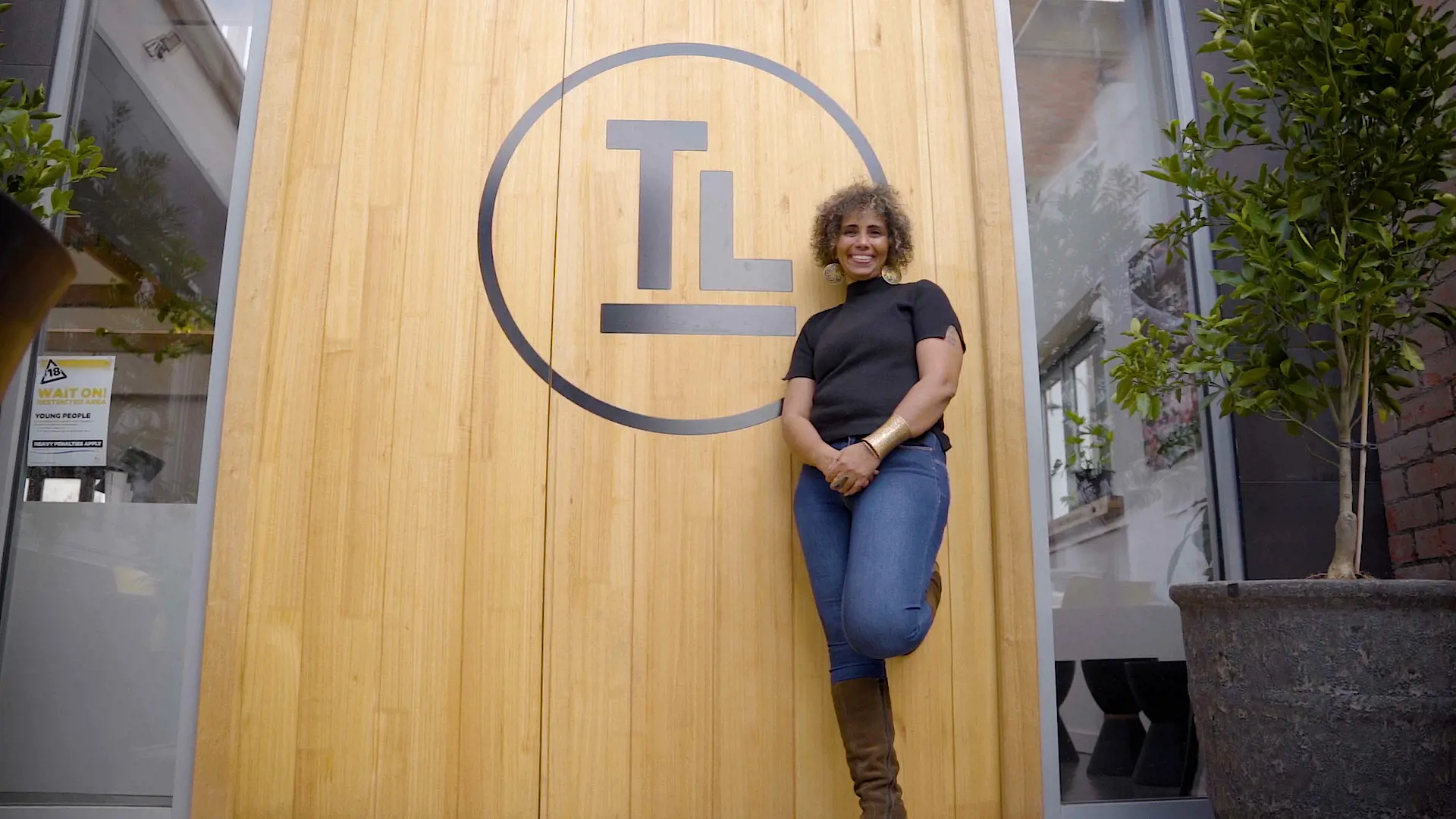 A woman stands at the front of a large, wooden door with a circular logo. 