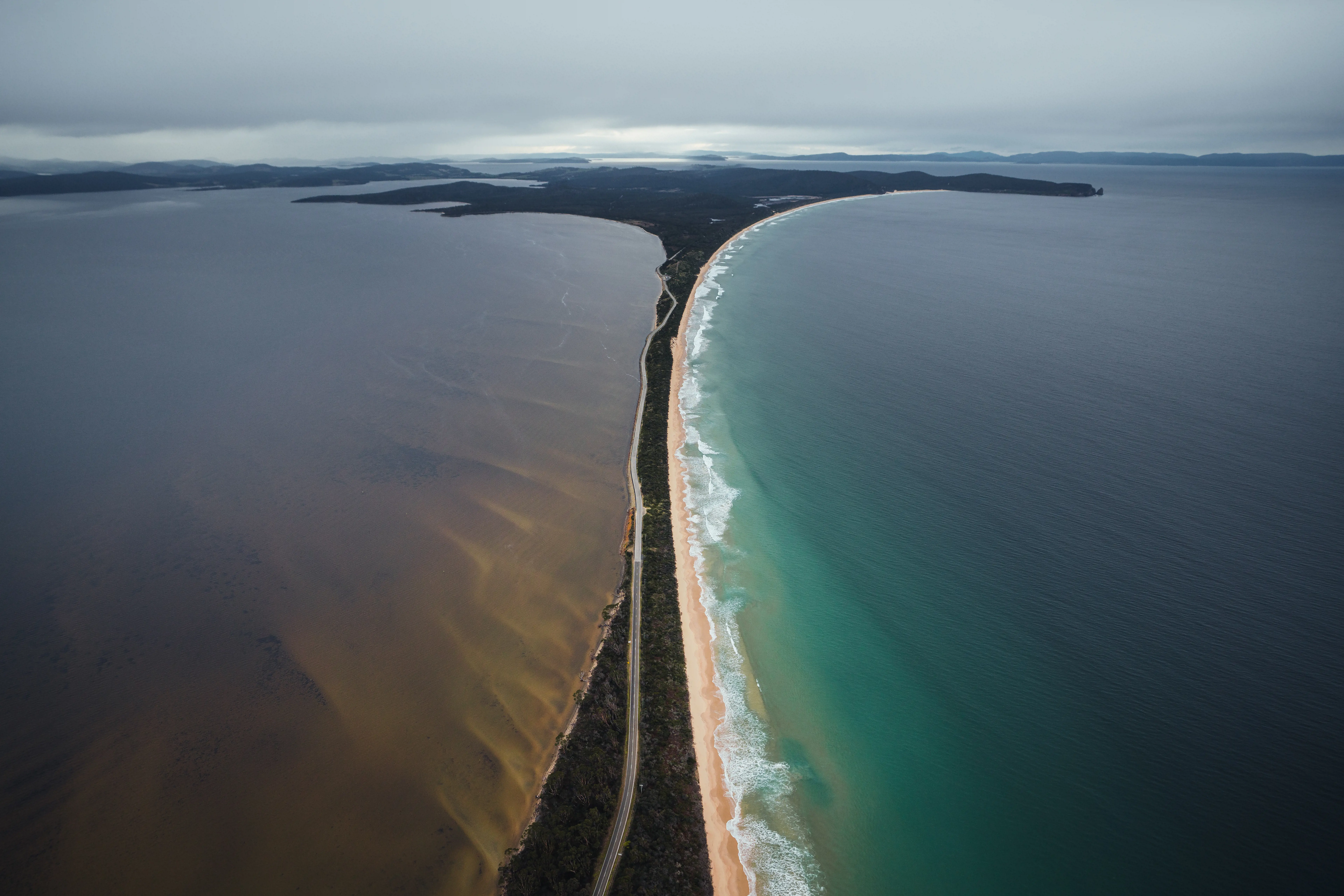 A narrow band of land joining two larger land masses divides the sea on an overcast day.