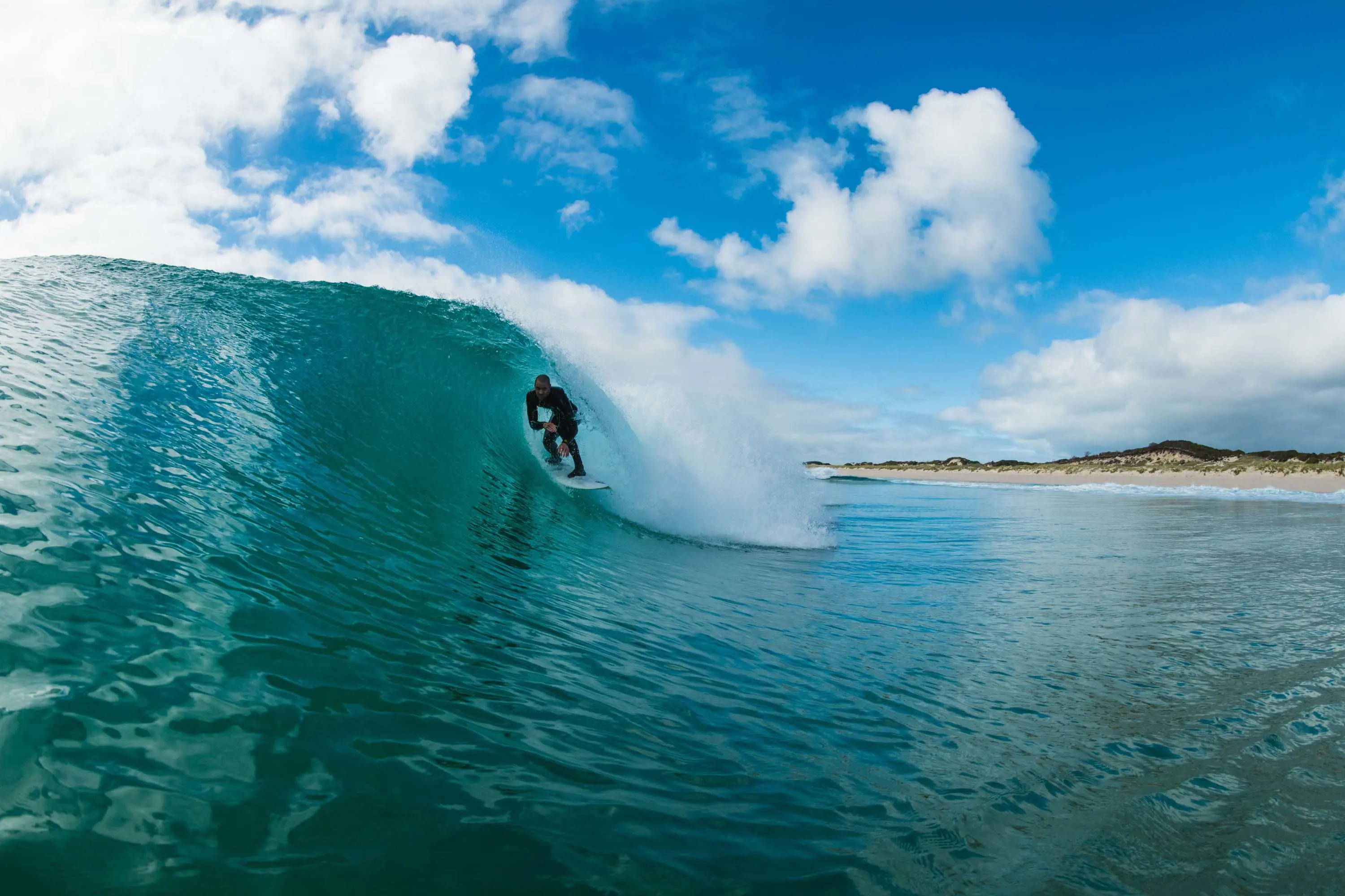 A man in a wetsuit crouches on a surfboard inside the barrel of a crashing wave.