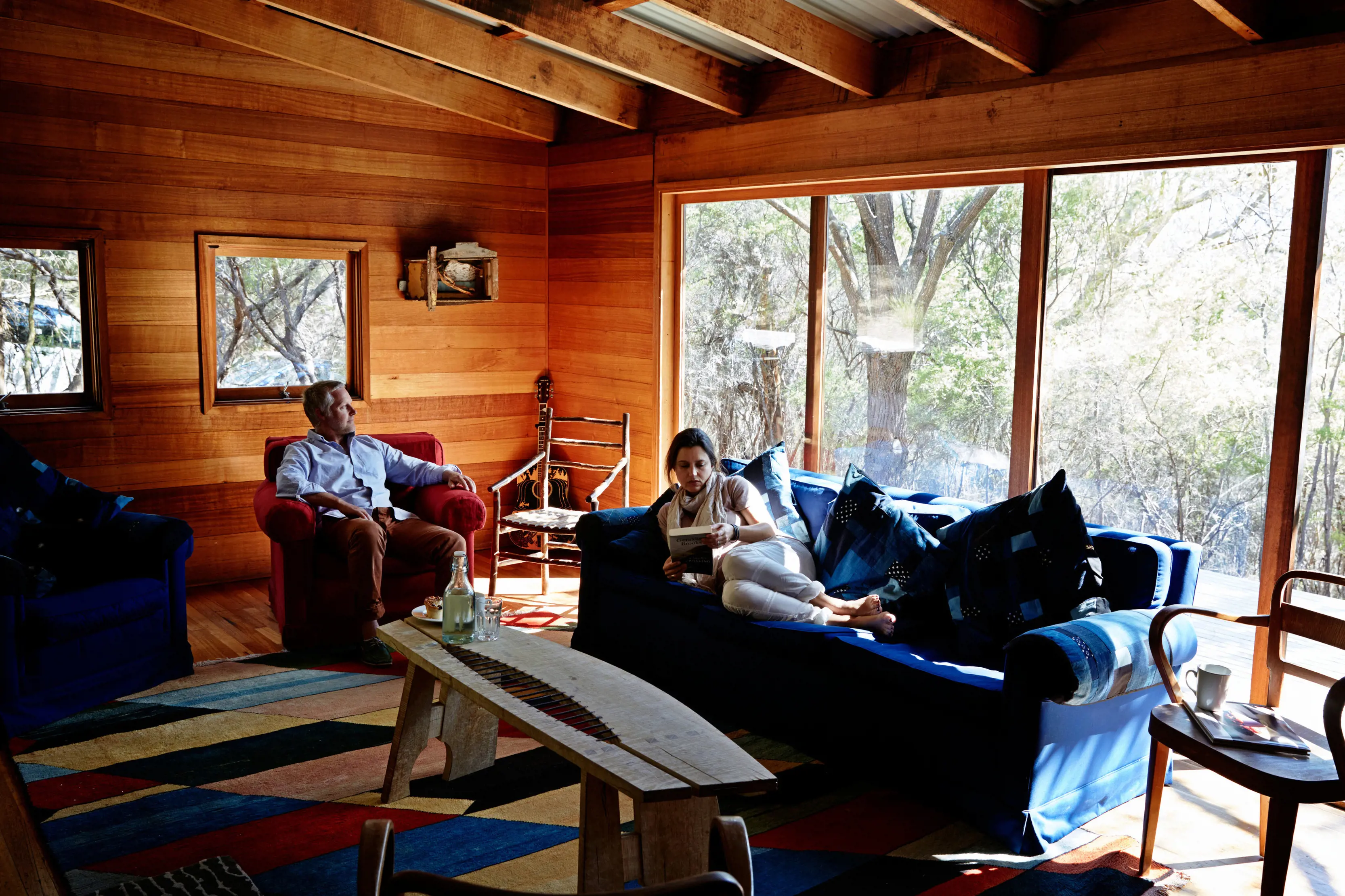 A couple rest inside Friendly Beaches Lodge accomodation, the sun beams through the glass window.