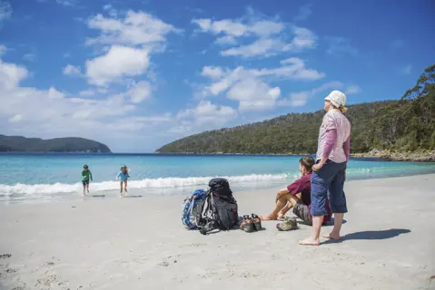 Children run from the sea towards their parents at Fortescue Bay, The Three Capes Track