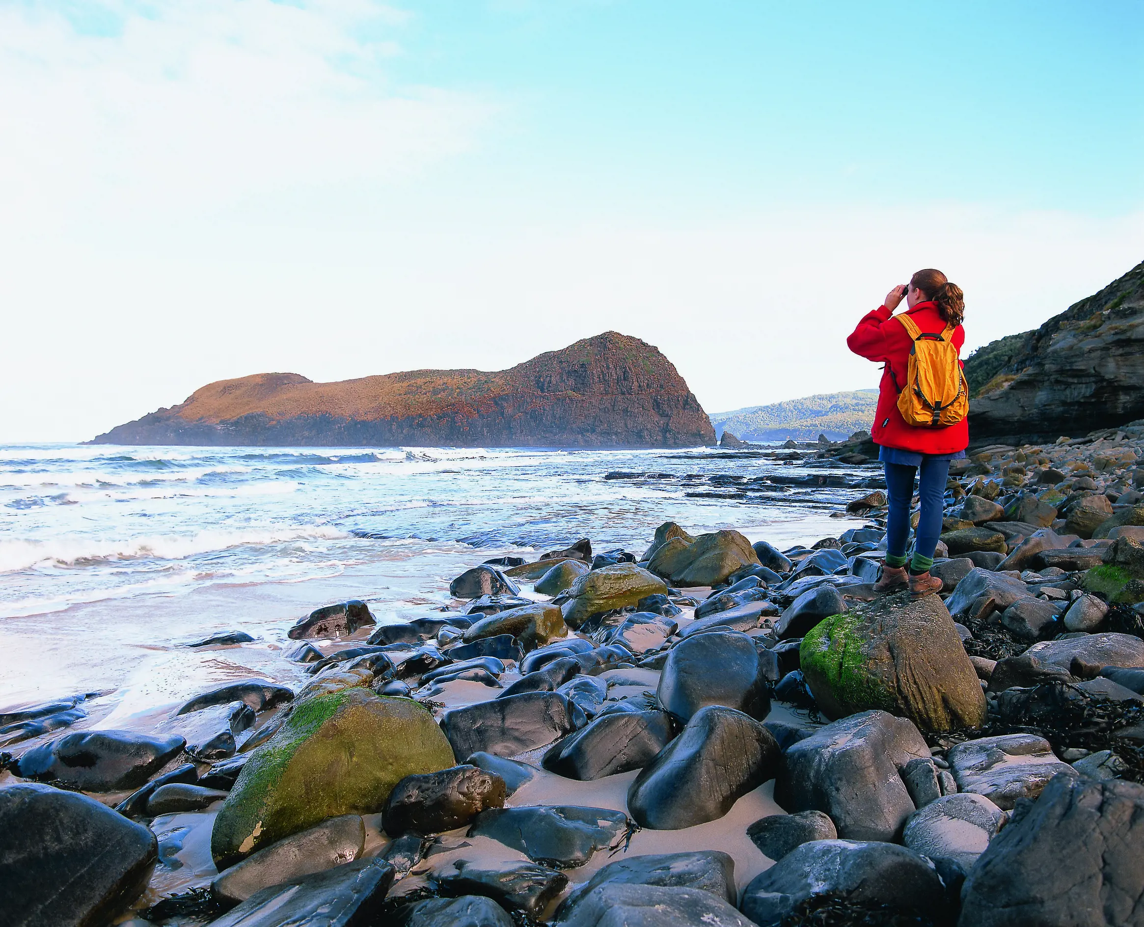 Woman standing on the rocks looking at the view from South Cape Bay - Cockle Creek