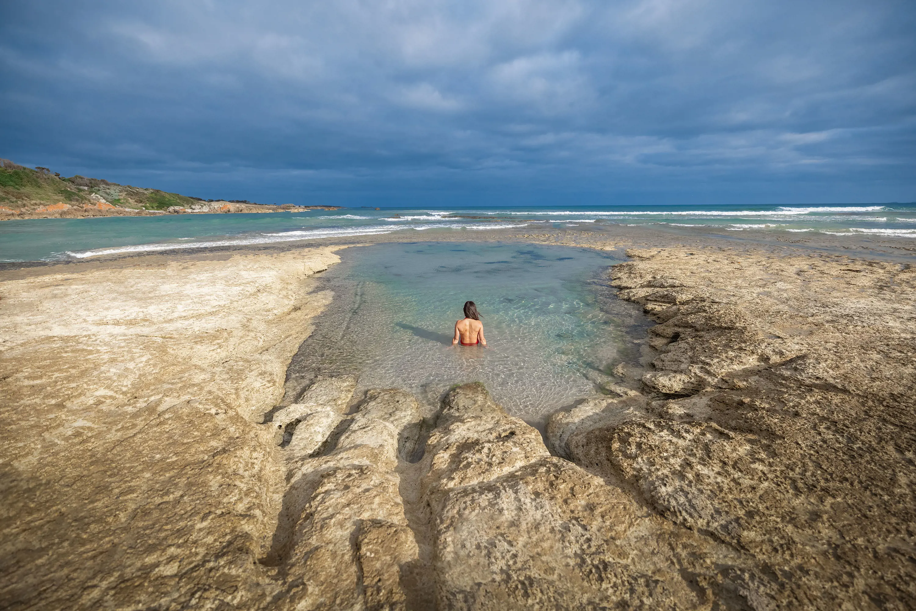 A woman relaxes in the clear water of a shallow rockpool.