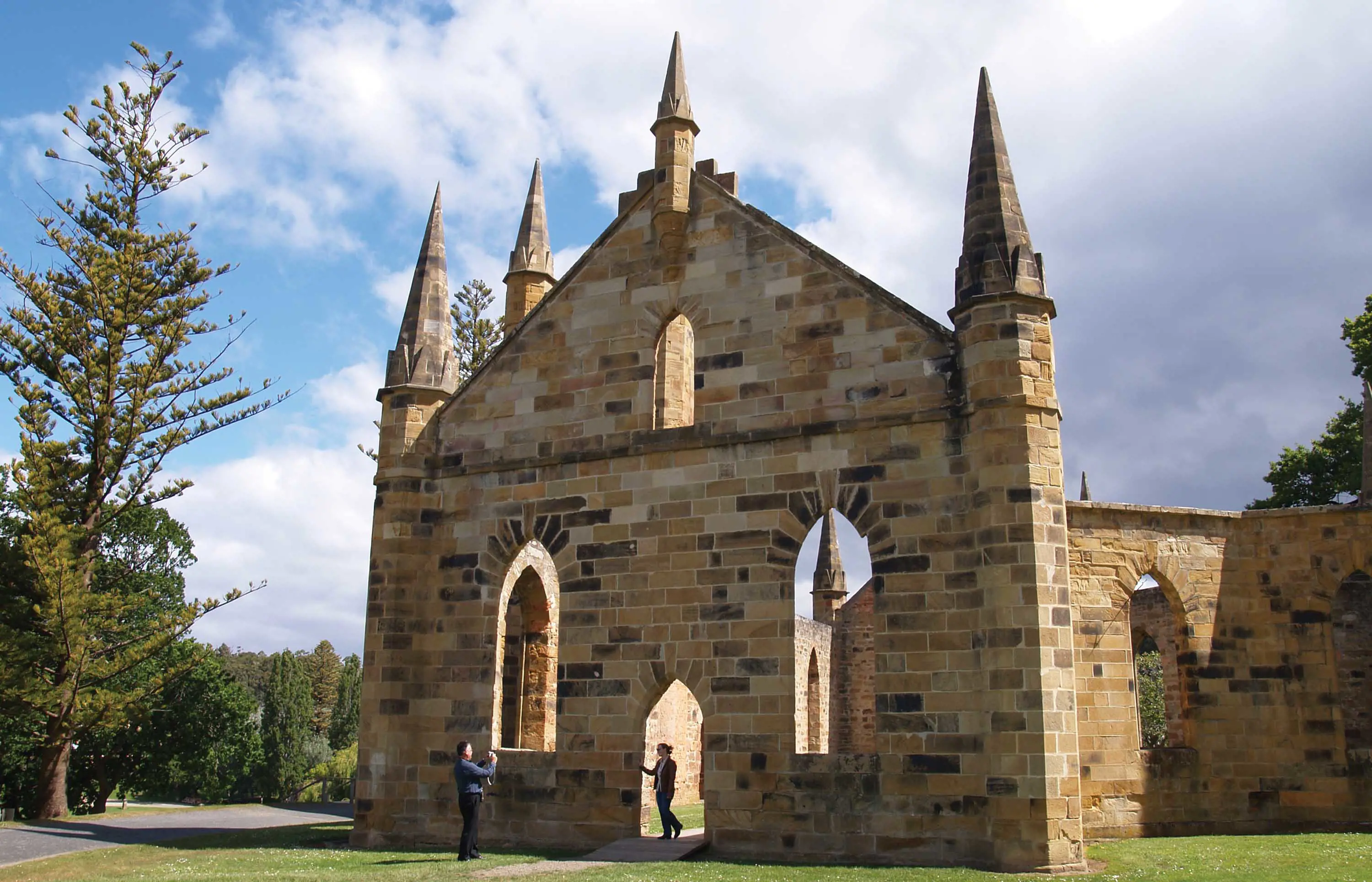 The stone façade of a historic church. A person stands in the archway of the entrance while another takes a photograph.