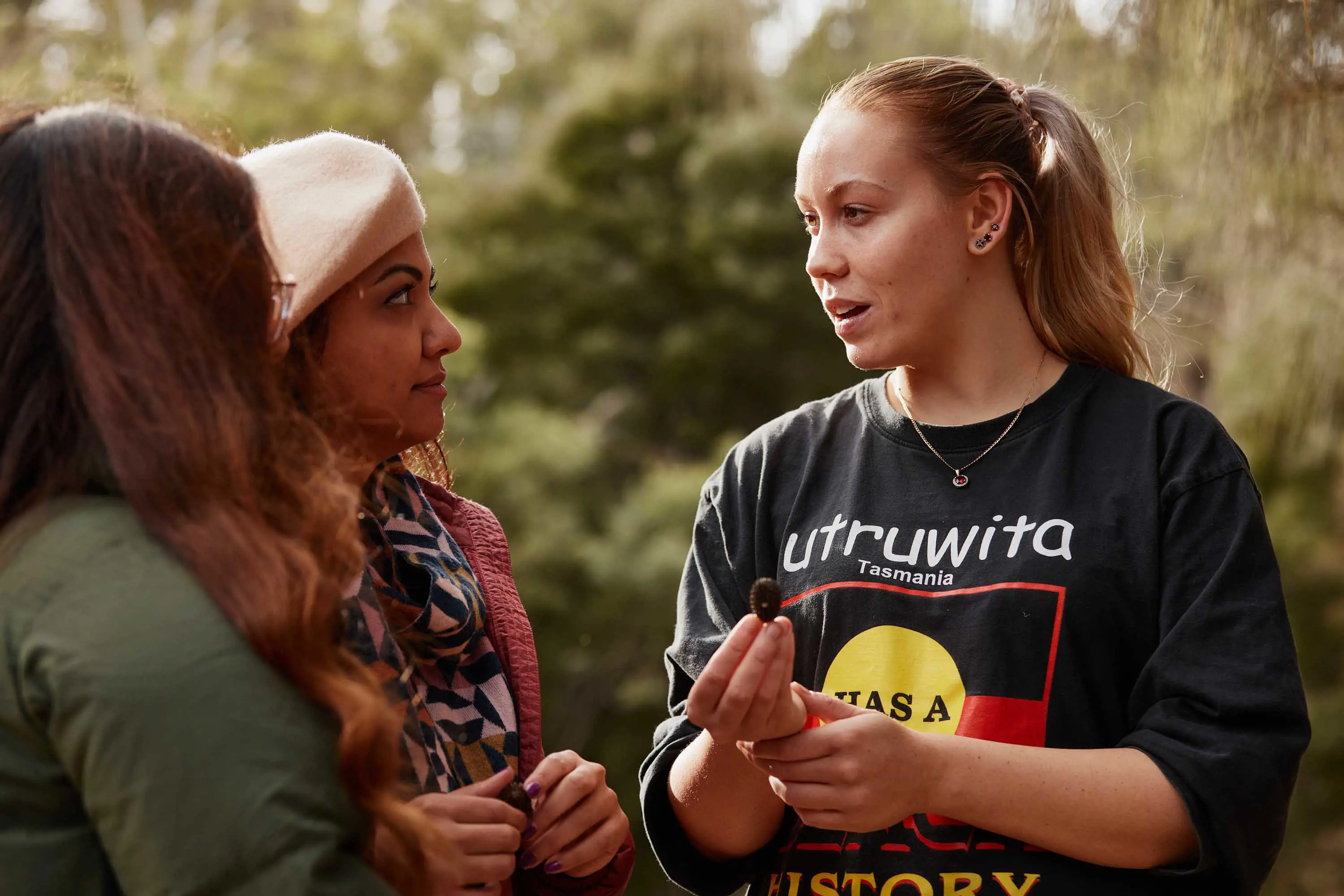 A young woman holds a small seed casing and talks with two other women.