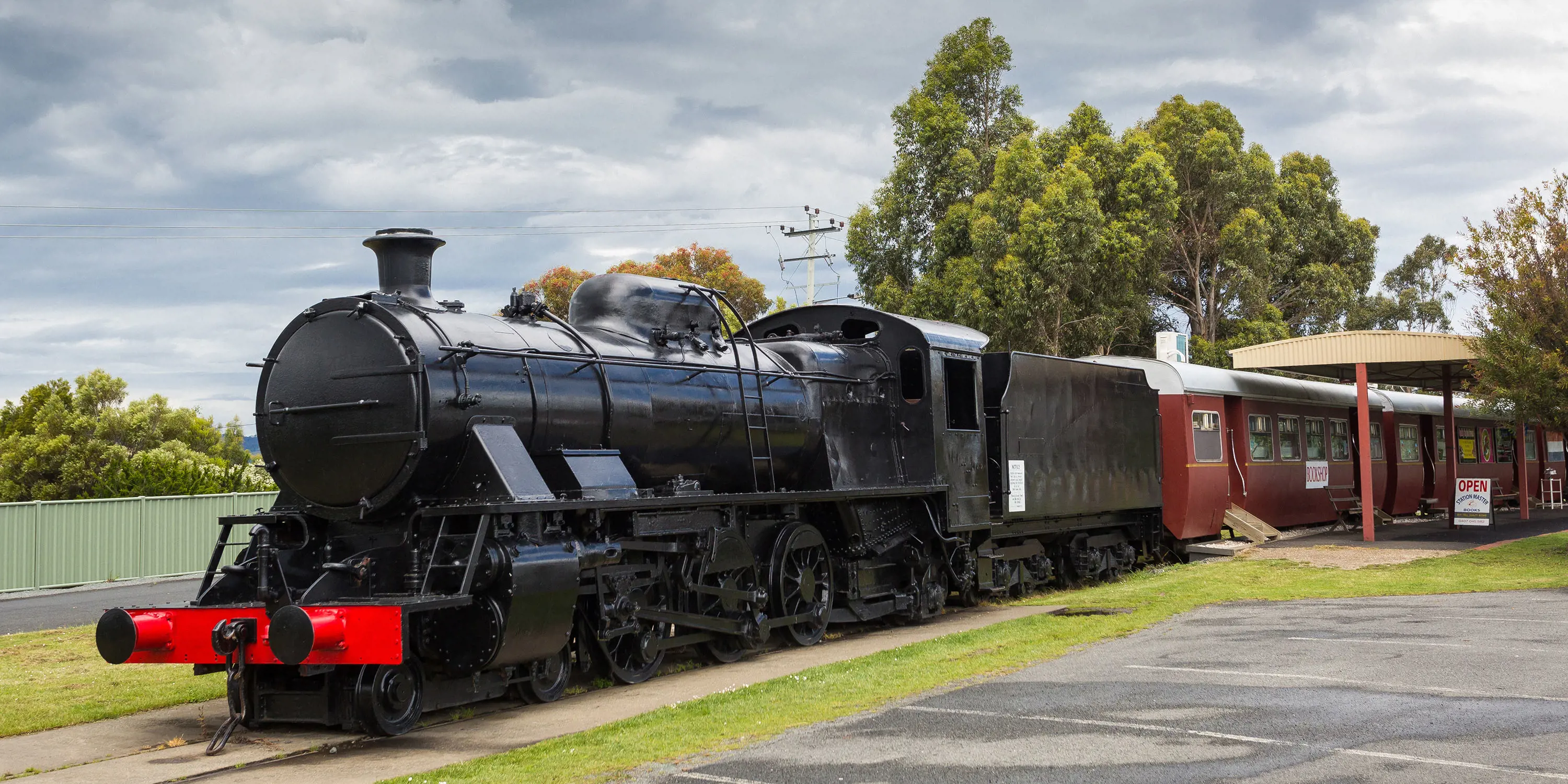 A large black steam engine sits stationary, with red carriages behind it that have been turned into shops with awnings and signs out the front.