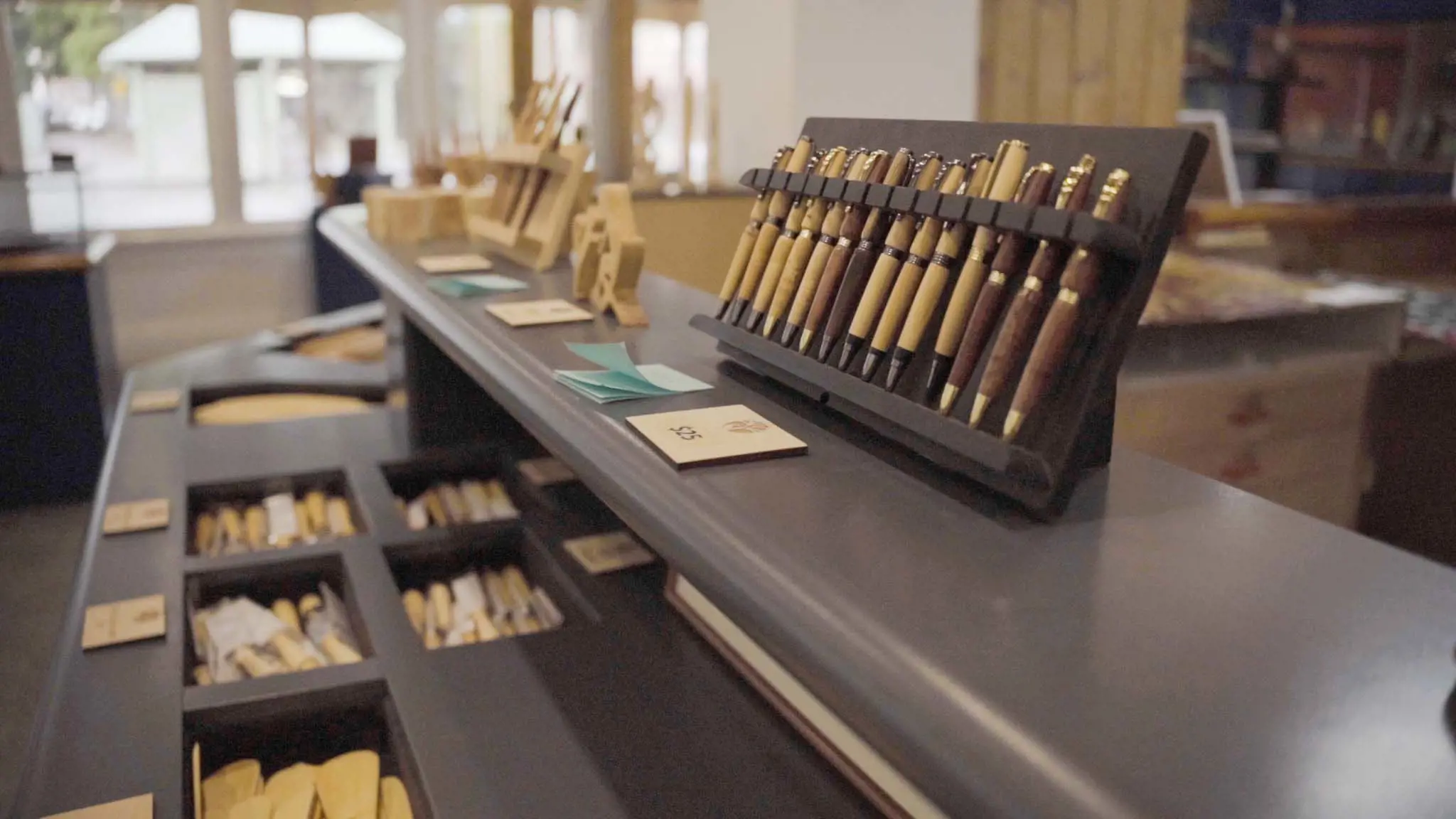 A display cabinet with a case of pens made from light-coloured wood, and other kitchen utensils made from similar materials.