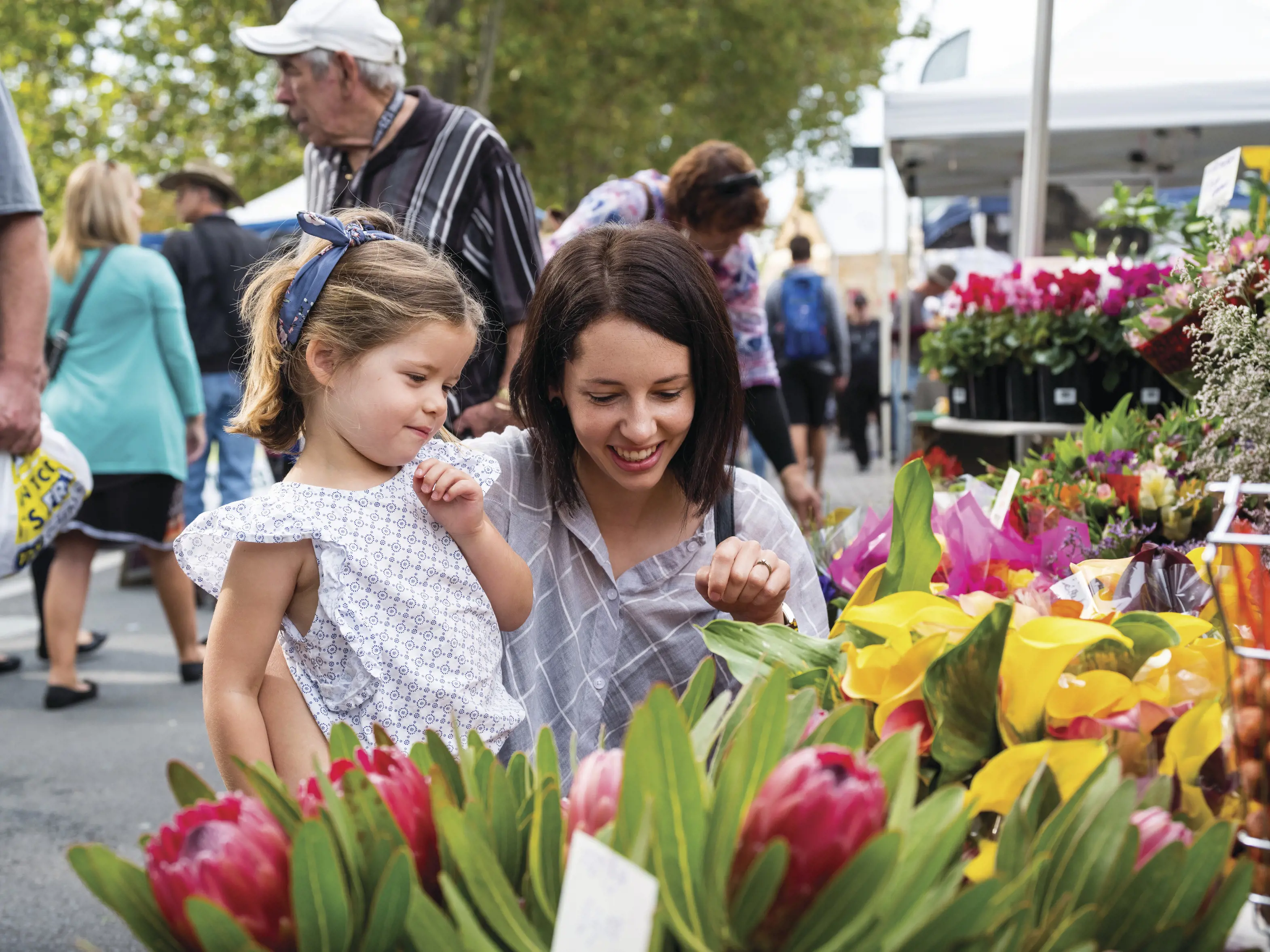 A mother and daughter crouched down looking at flowers at Salamanca Market.