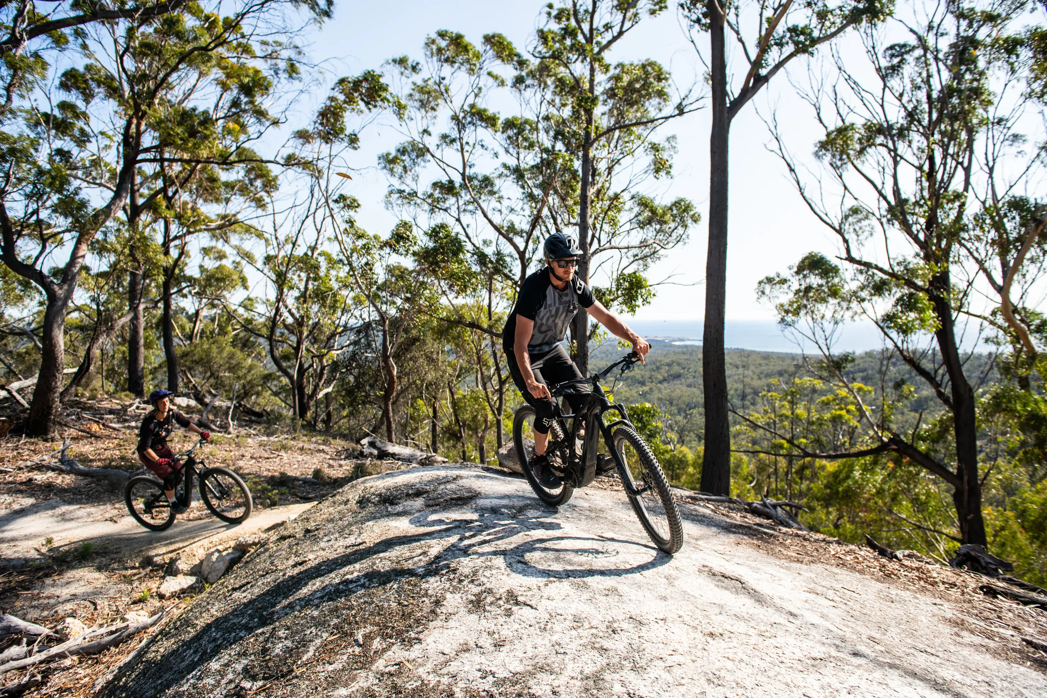 Cyclists at the top of St Helens Mountain Bike Trails, with rainforest views in the background.