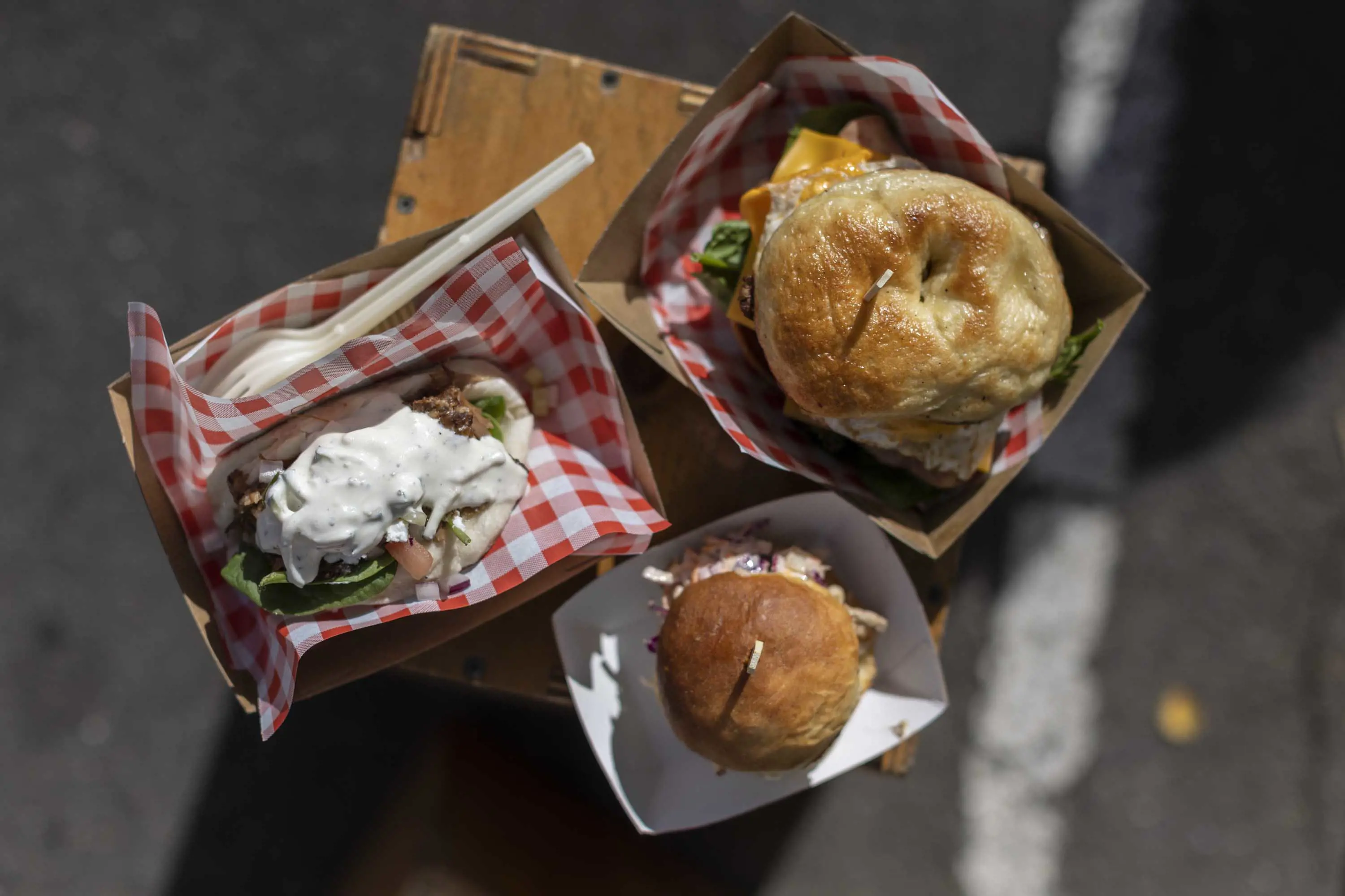 A homemade burger, brioche and salad taco in cardboard trays and red checkered napkins.