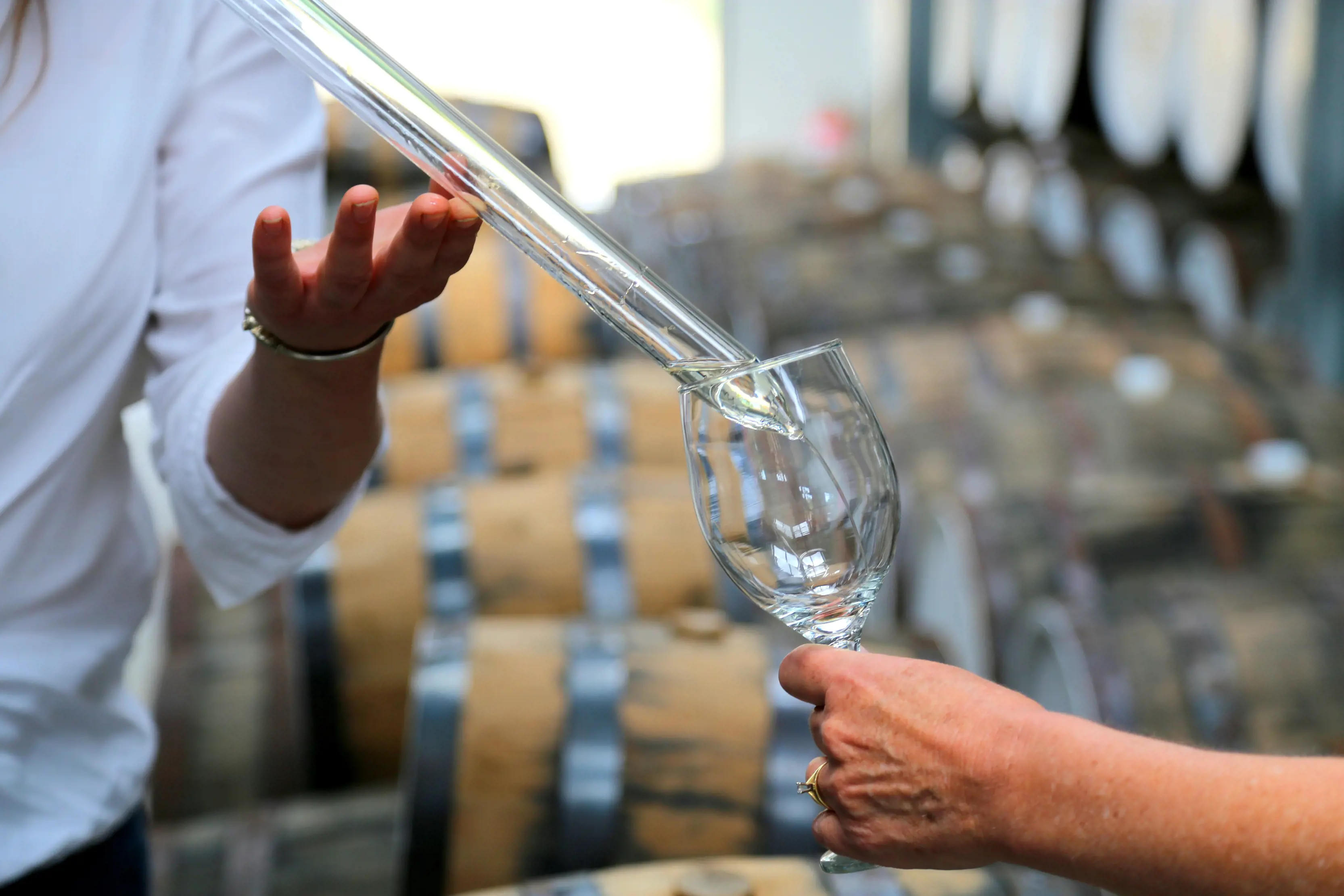 Close up of gin being poured into a glass through a tube at McHenry Distillery, with barrels in the background.