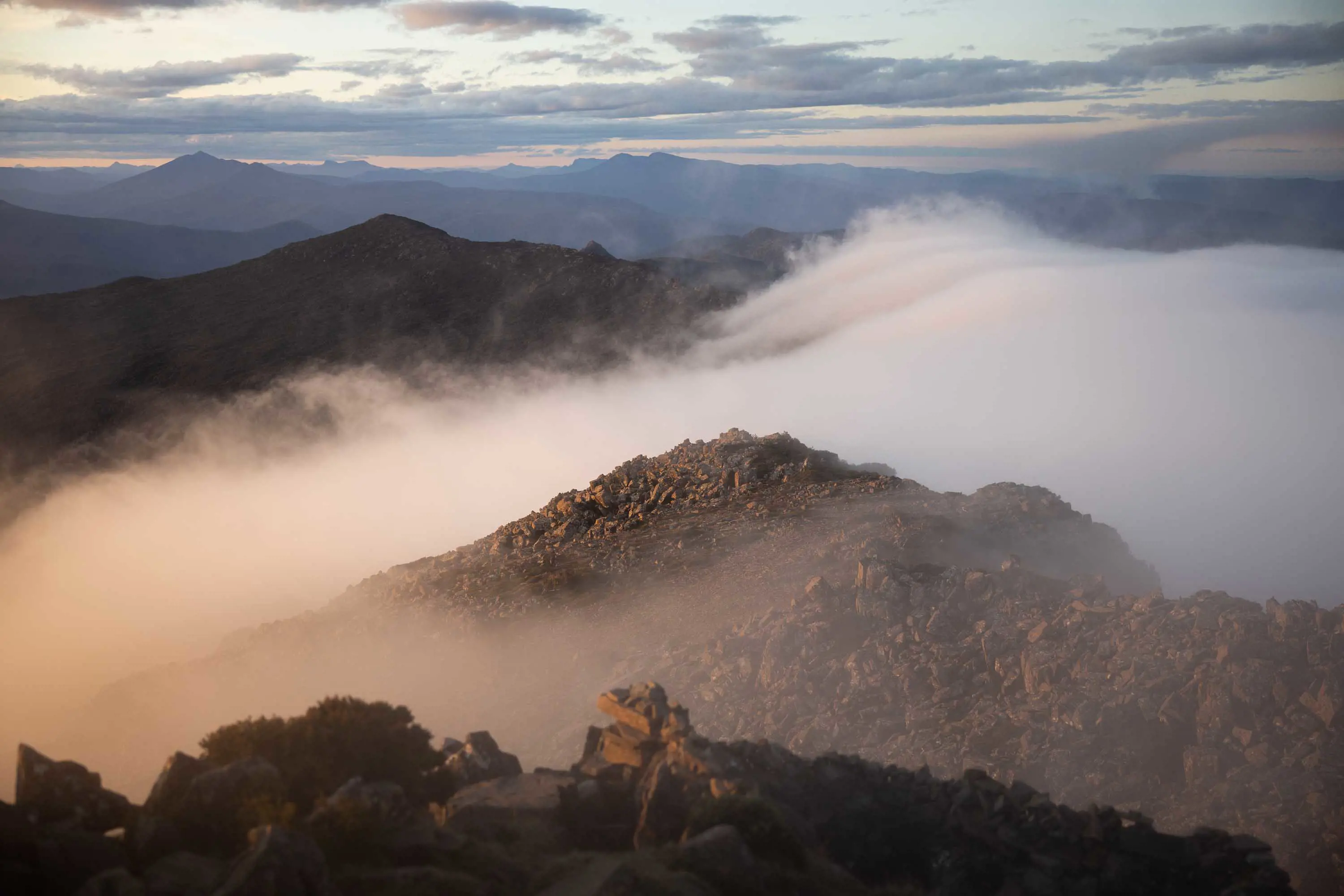 A rock mountain range, half covered in thick white, low-hanging cloud stretches out into the distance.