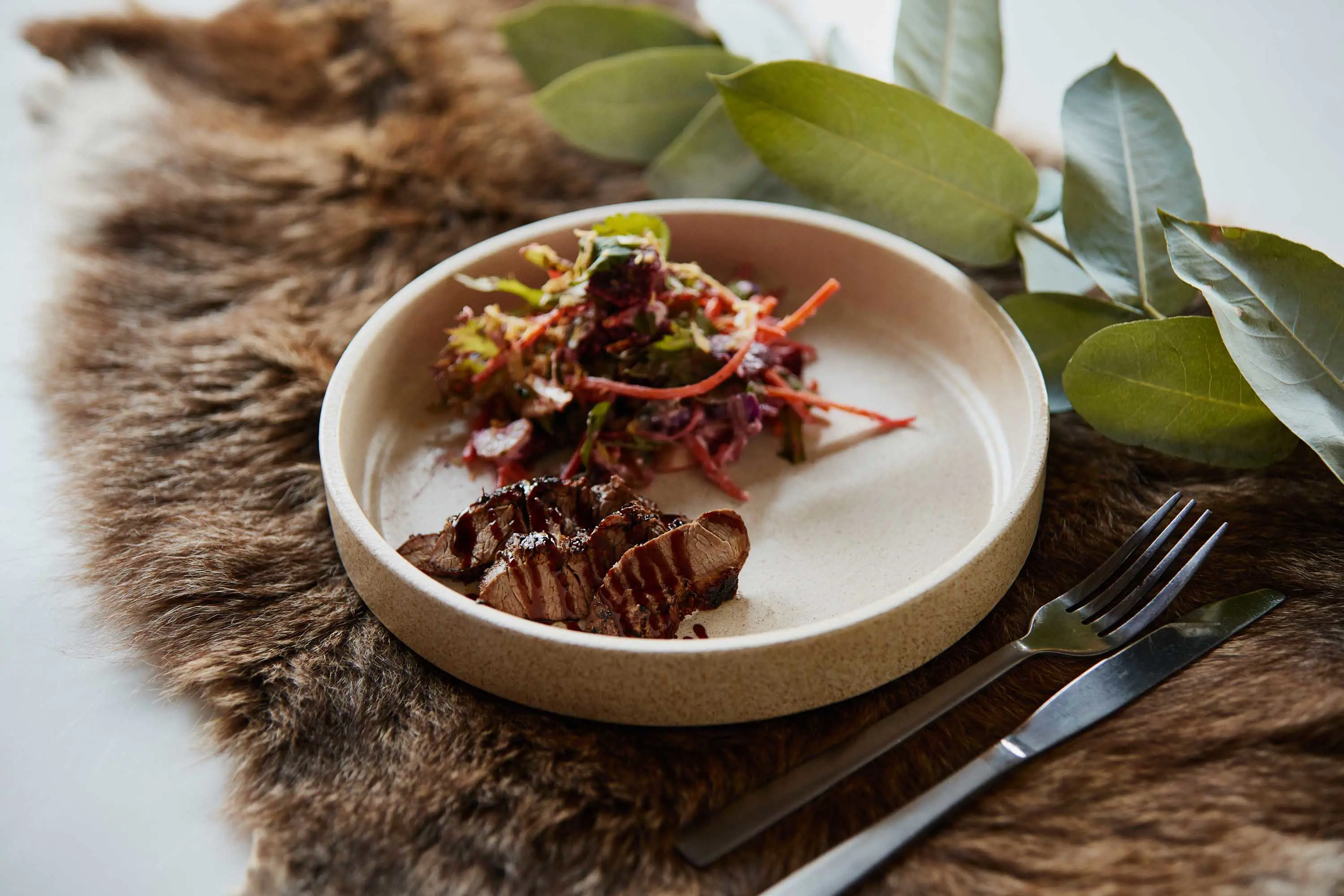 A dish of cooked meat and vegetables presented on a fur with silver cutlery.