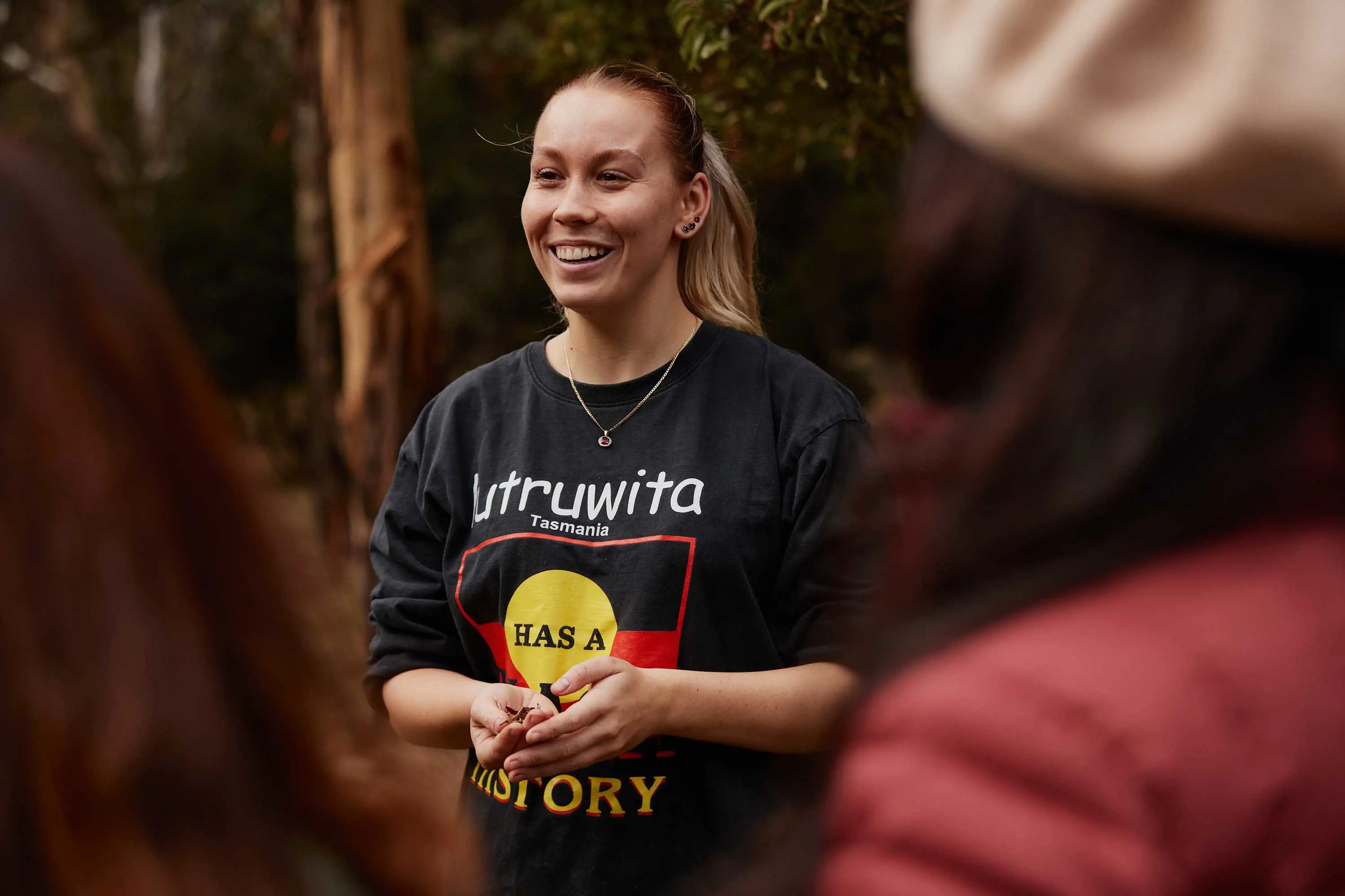 A young woman talks with guests standing in the shade of a tree.