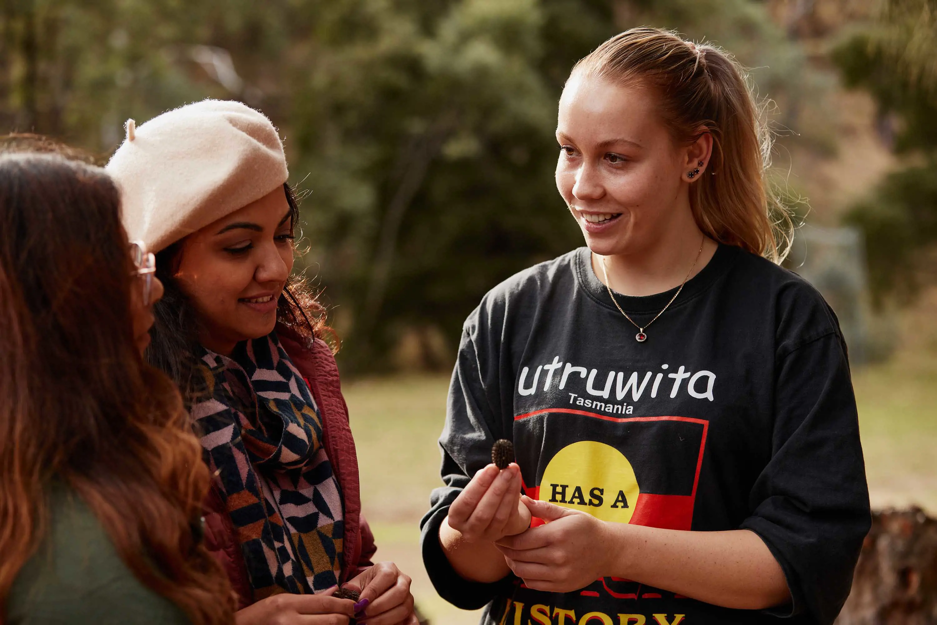 A young woman holds a small seed pod and talks about it with guests on a tour outdoors.