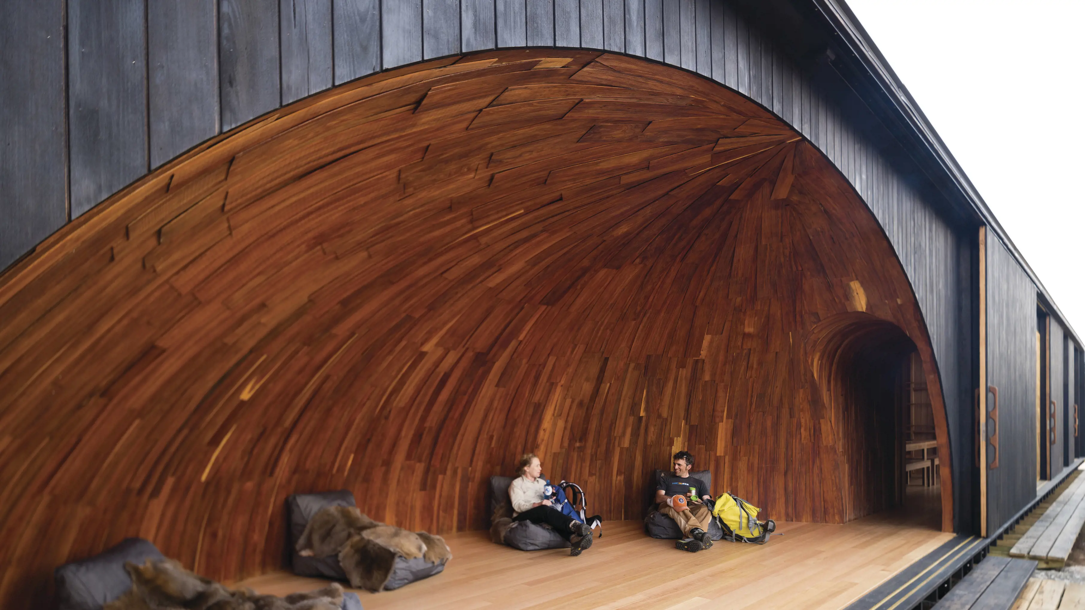 Three people sit under an alcove in a building which is part of The Wukalina Walk, an Aboriginal owned and operated guided walk.