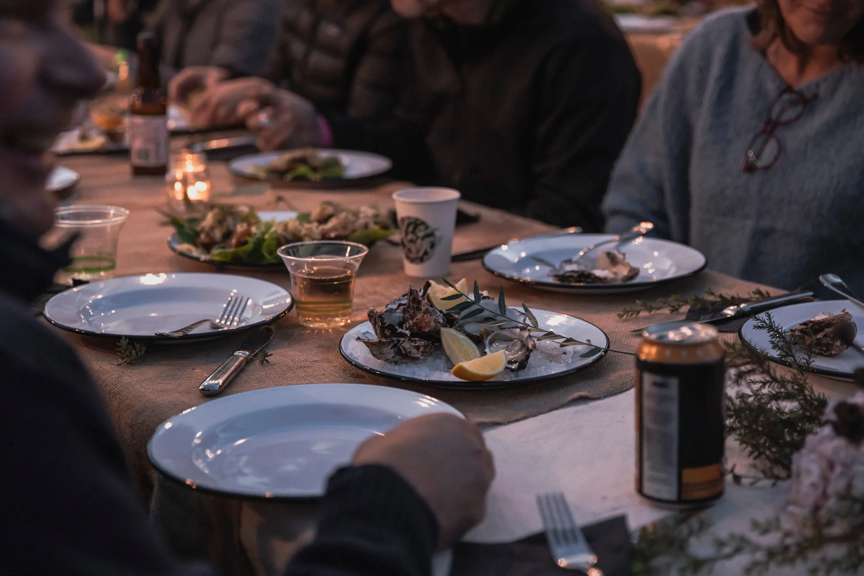 People seated at a long table set rustically, ready to eat the food from shared plates in the middle.