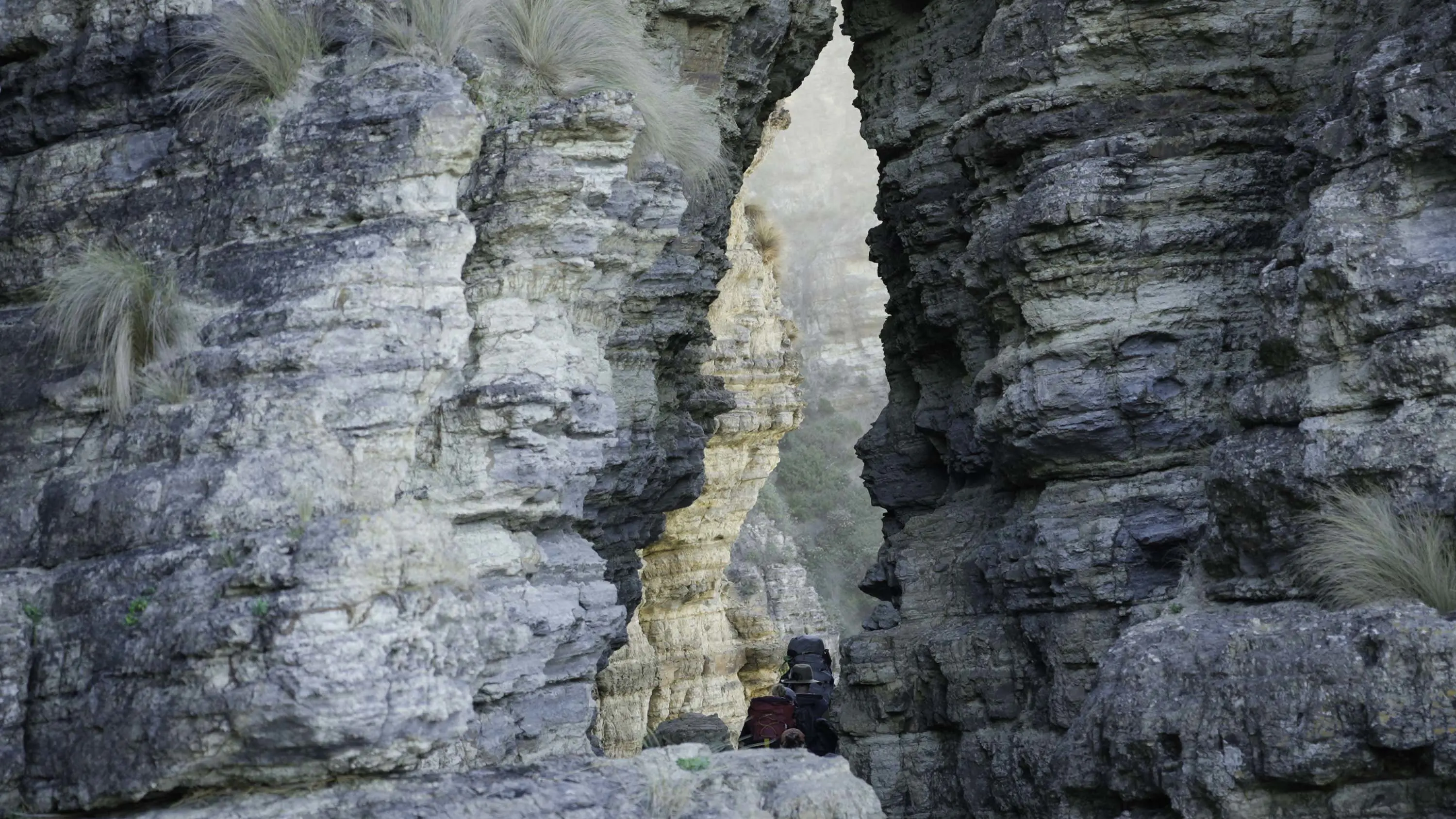 Sharp and craggy blue-yellow rock formations with an undulating space in between, through which a few hikers can be seen.