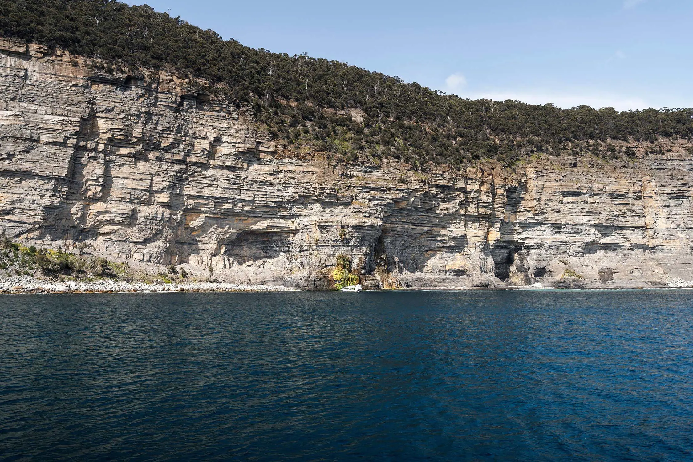 A sharp cliff face over some inky blue water.