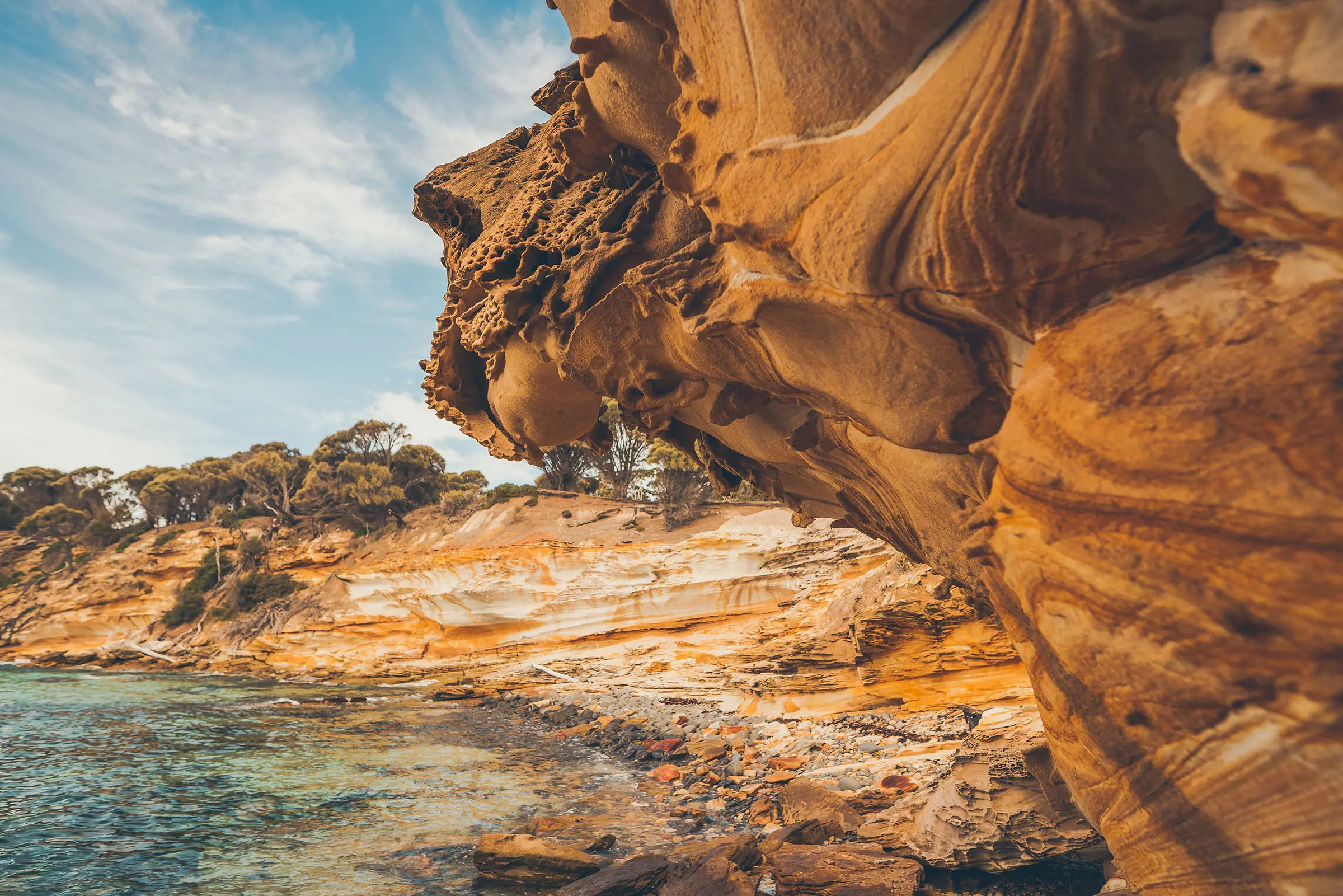 A cliff face overlooking the water shows swirling patterns in shades of orange sandstone.