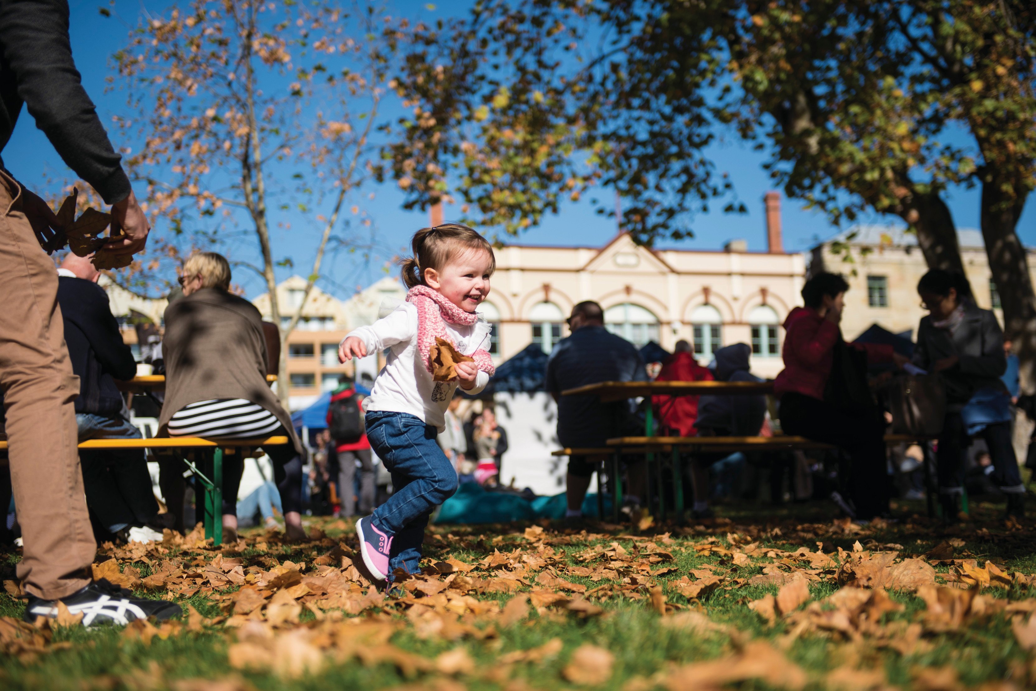 A little girl playing amongst the leaves at Salamanca Market. 