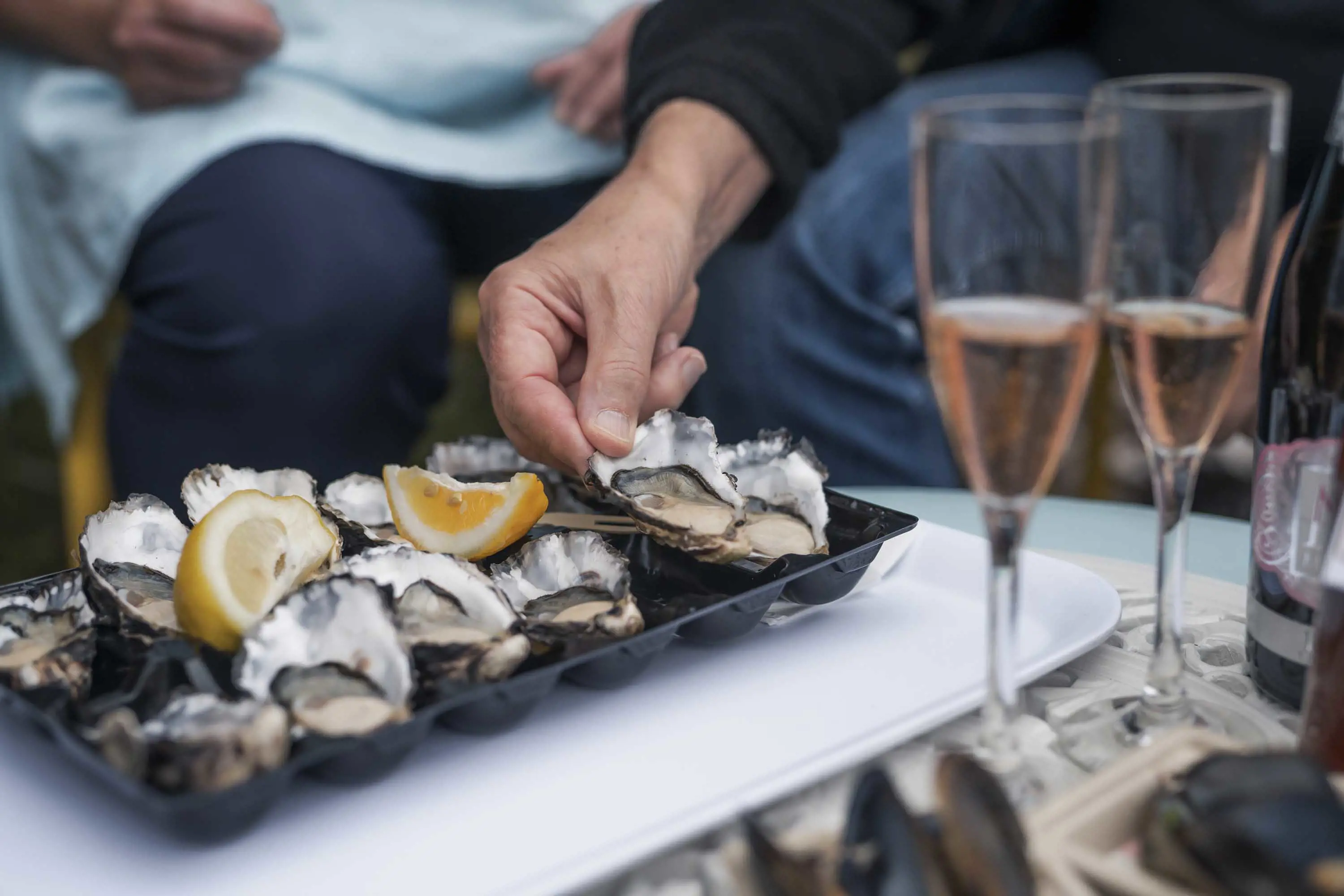 A man picks up an oyster in it's shell from a tray sitting on a table.