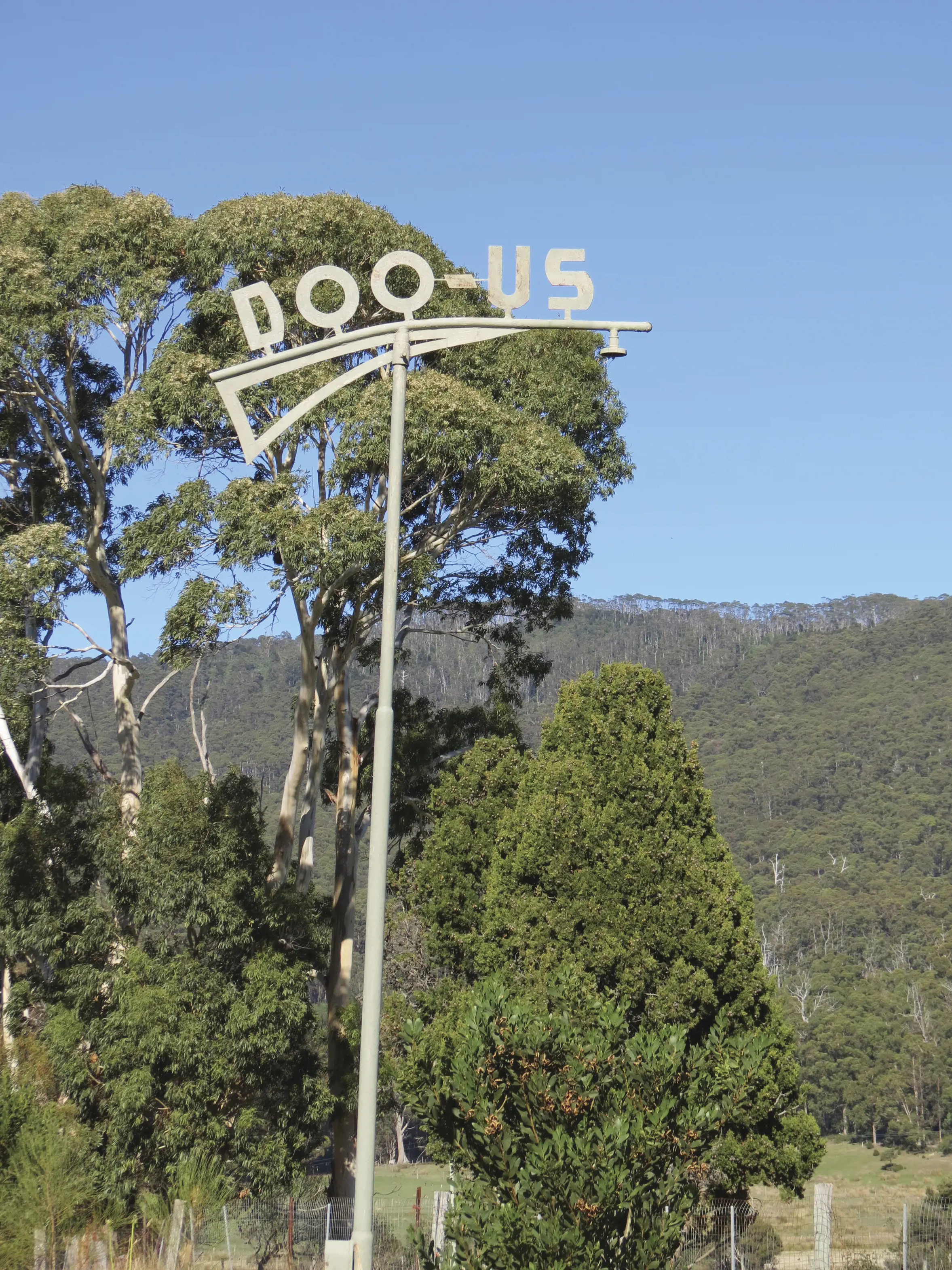 A tall metal streetlight with the letters 'Doo-Us' atop it.