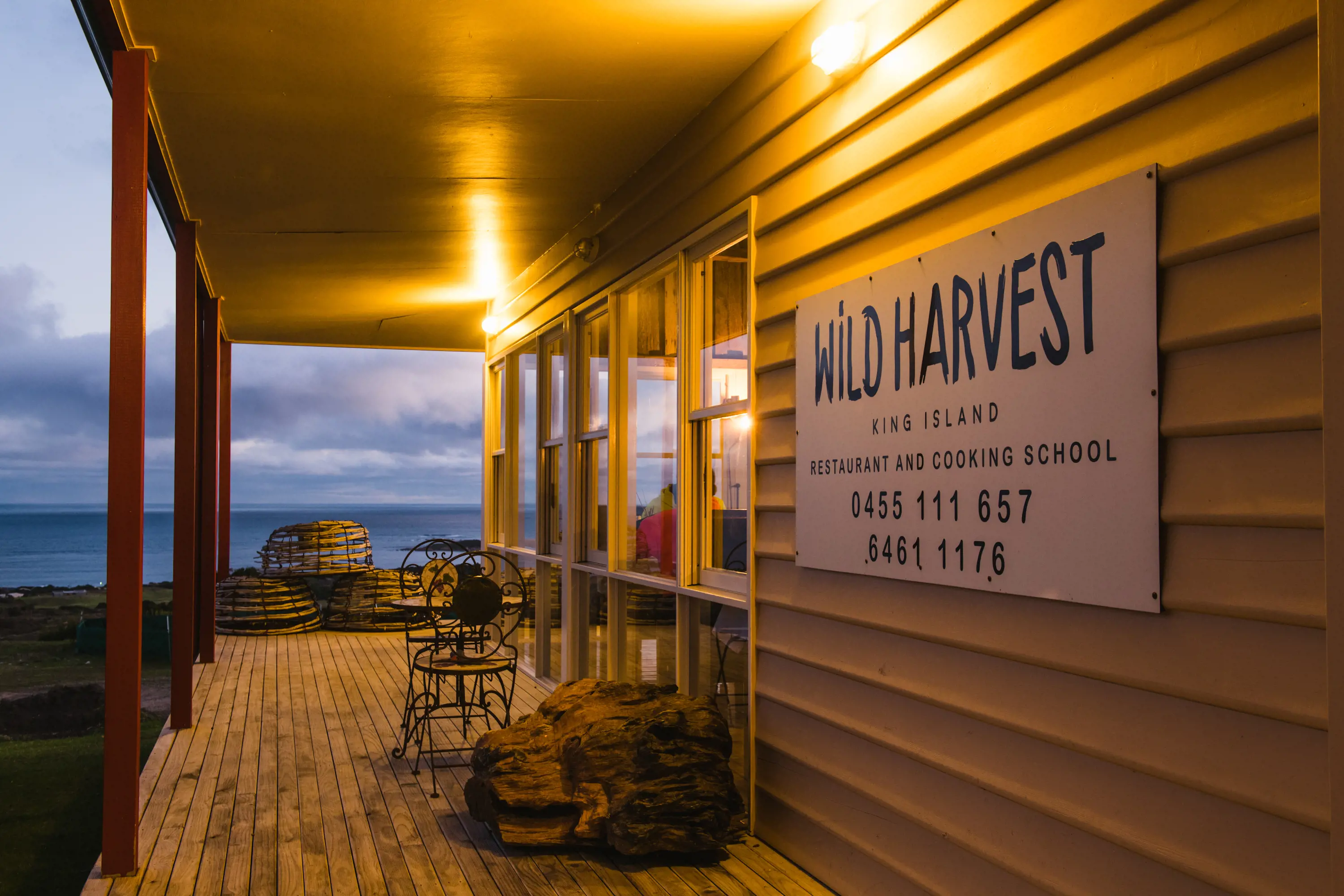 The lit exterior of a building's deck at dusk. A sign on the wall says 'Wild Harvest'. 