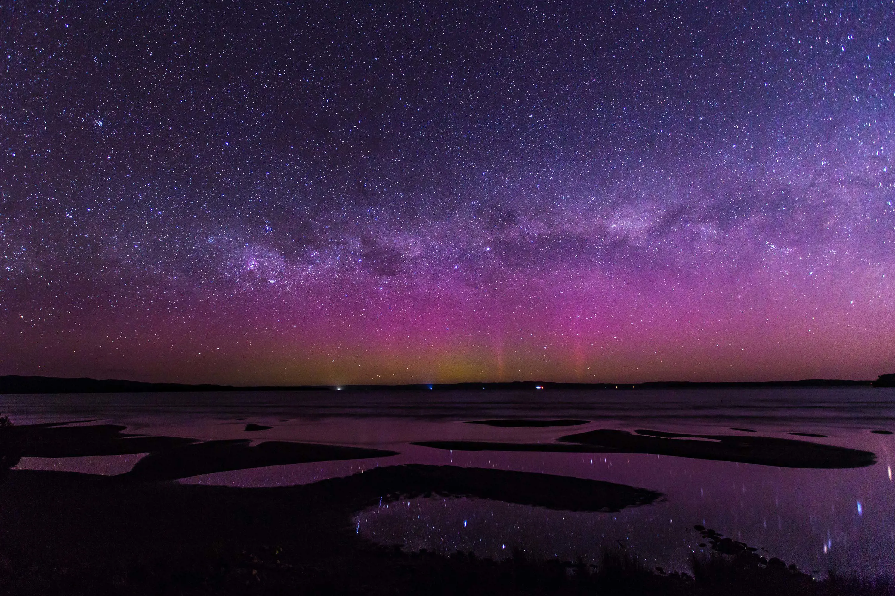 A stunning night sky with the aurora australis and stars reflected onto water undulating around sand bars.