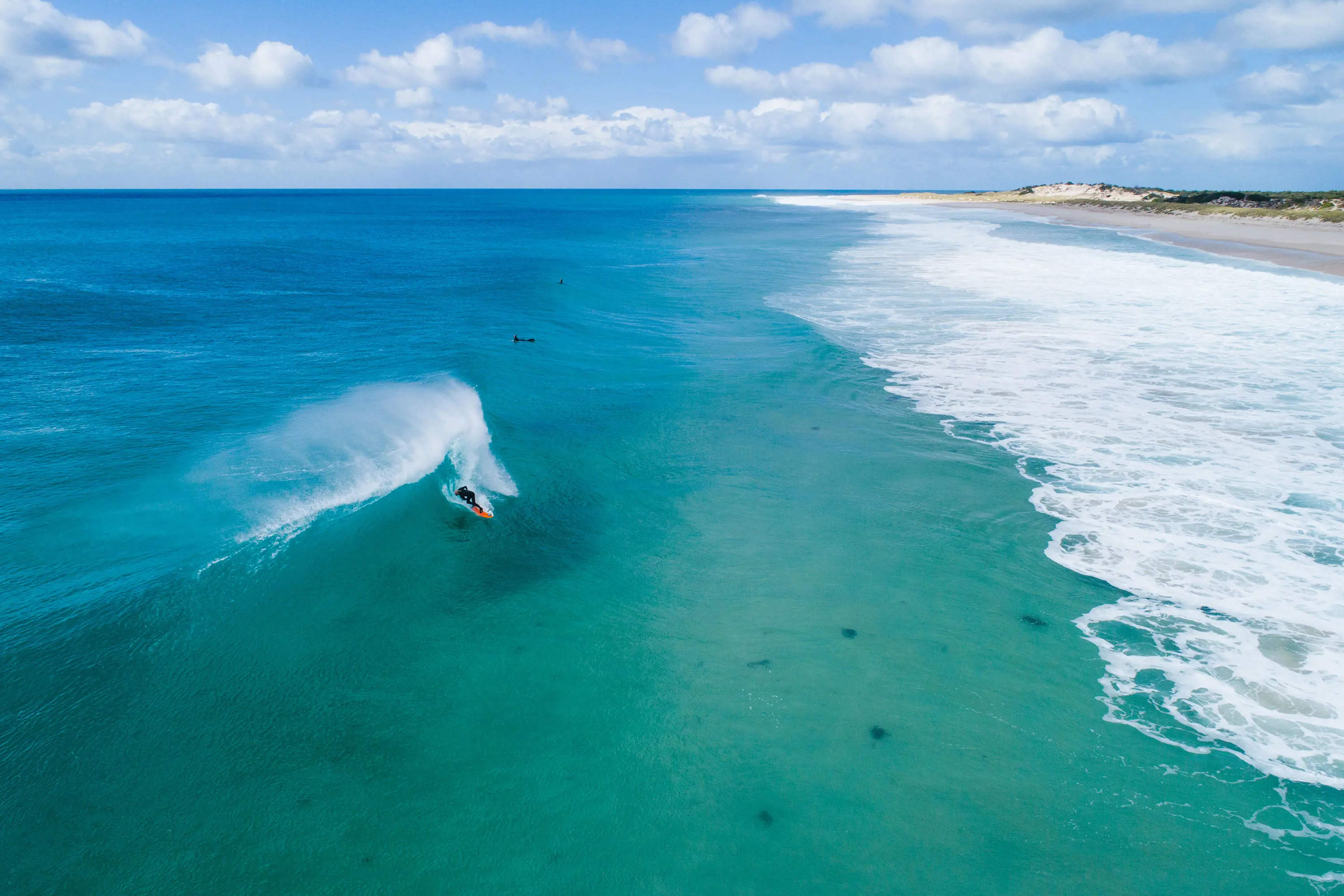 Stunning aerial image taken of a surfer pulling into a crystal blue, hollow wave on a clear, sunny morning.