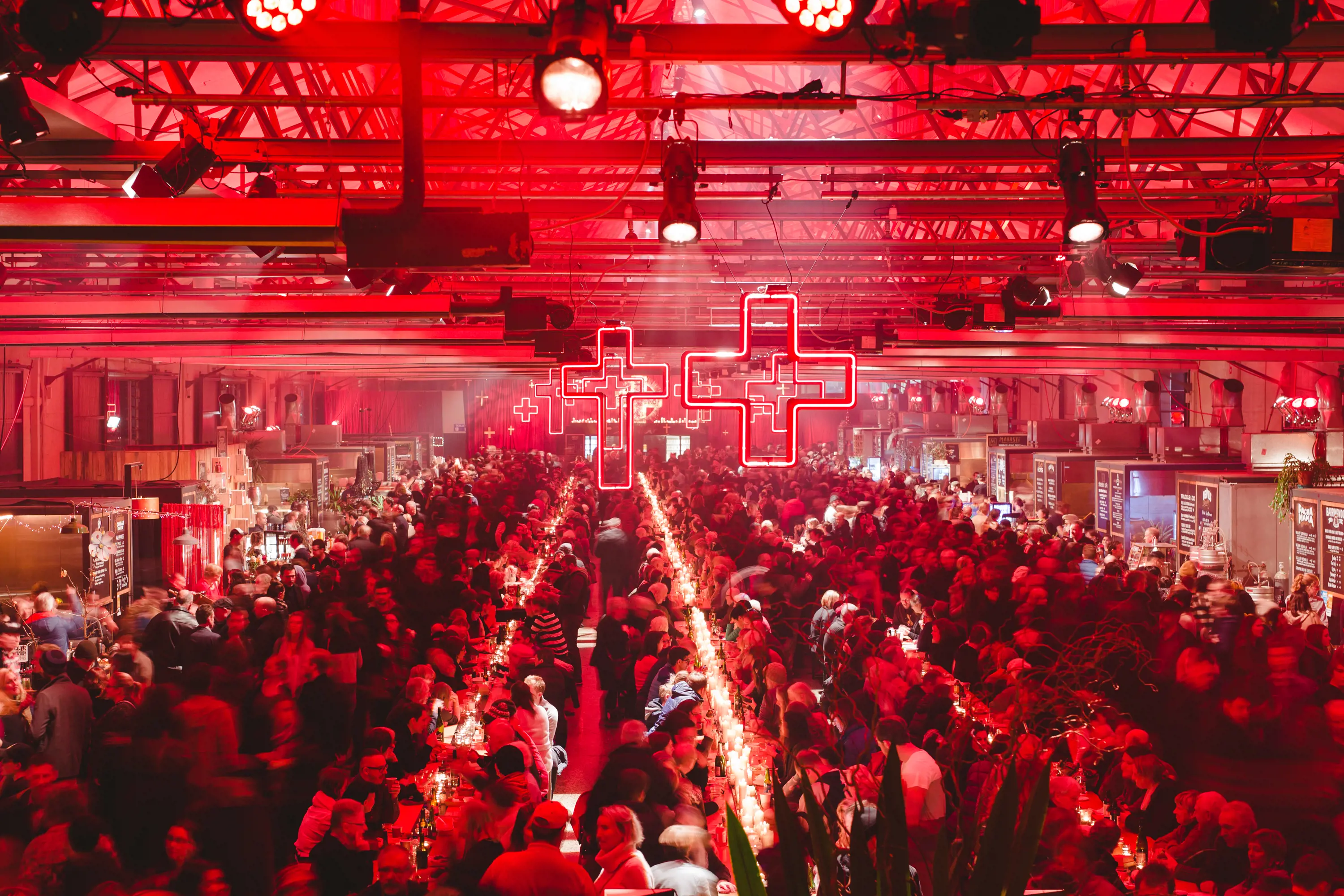 a large dock shed with high ceilings converted into a dinning hall with red lighting and thousands of people sitting at long tables.