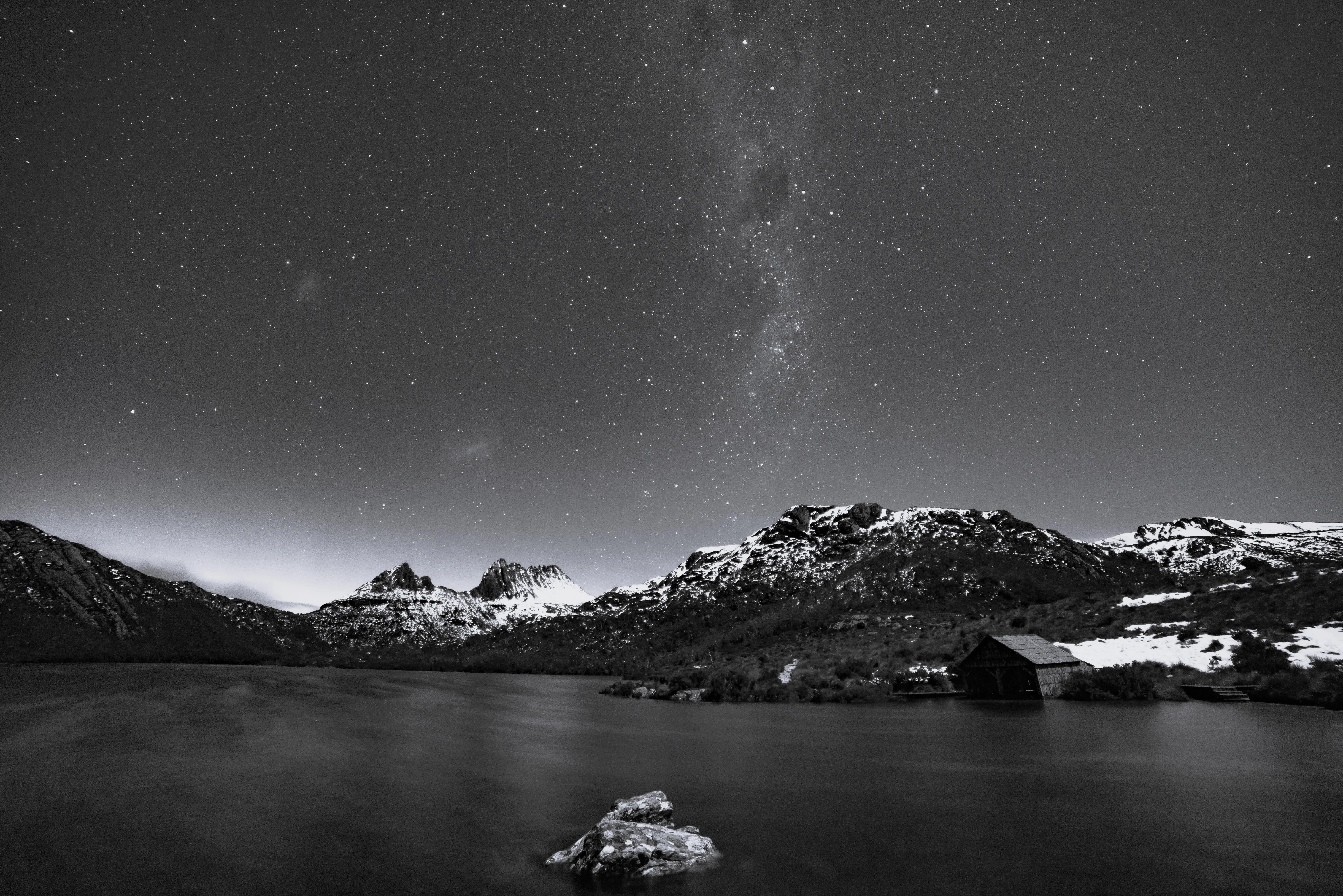 A large lake and a snow-capped mountain under a star-filled night sky. 