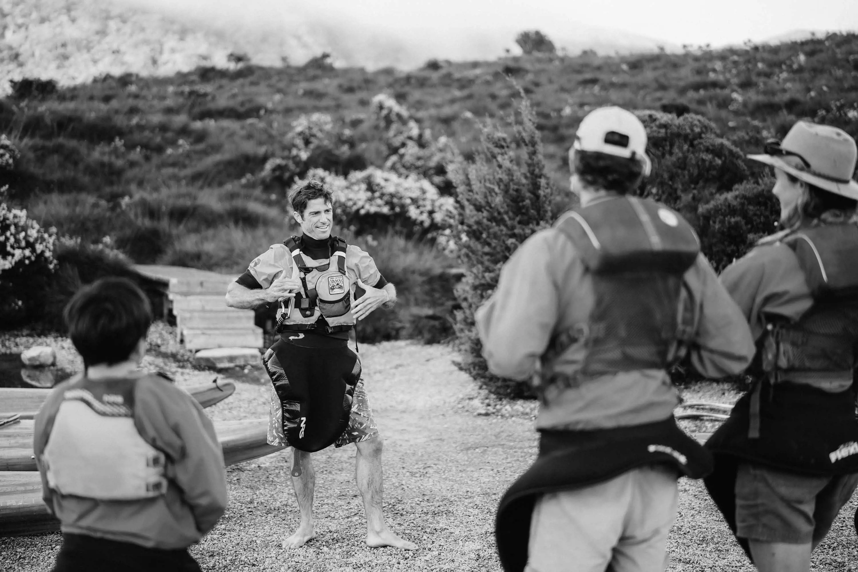 A man wearing a wetsuit stands in front of a group people wearing lifejackets.