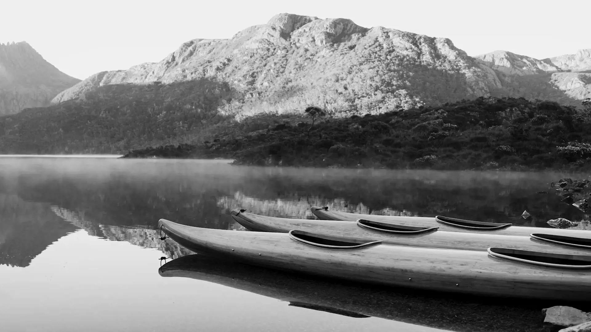 Wooden kayaks float on still, crystal-clear water on Dove Lake, with snow-covered mountain in the background.