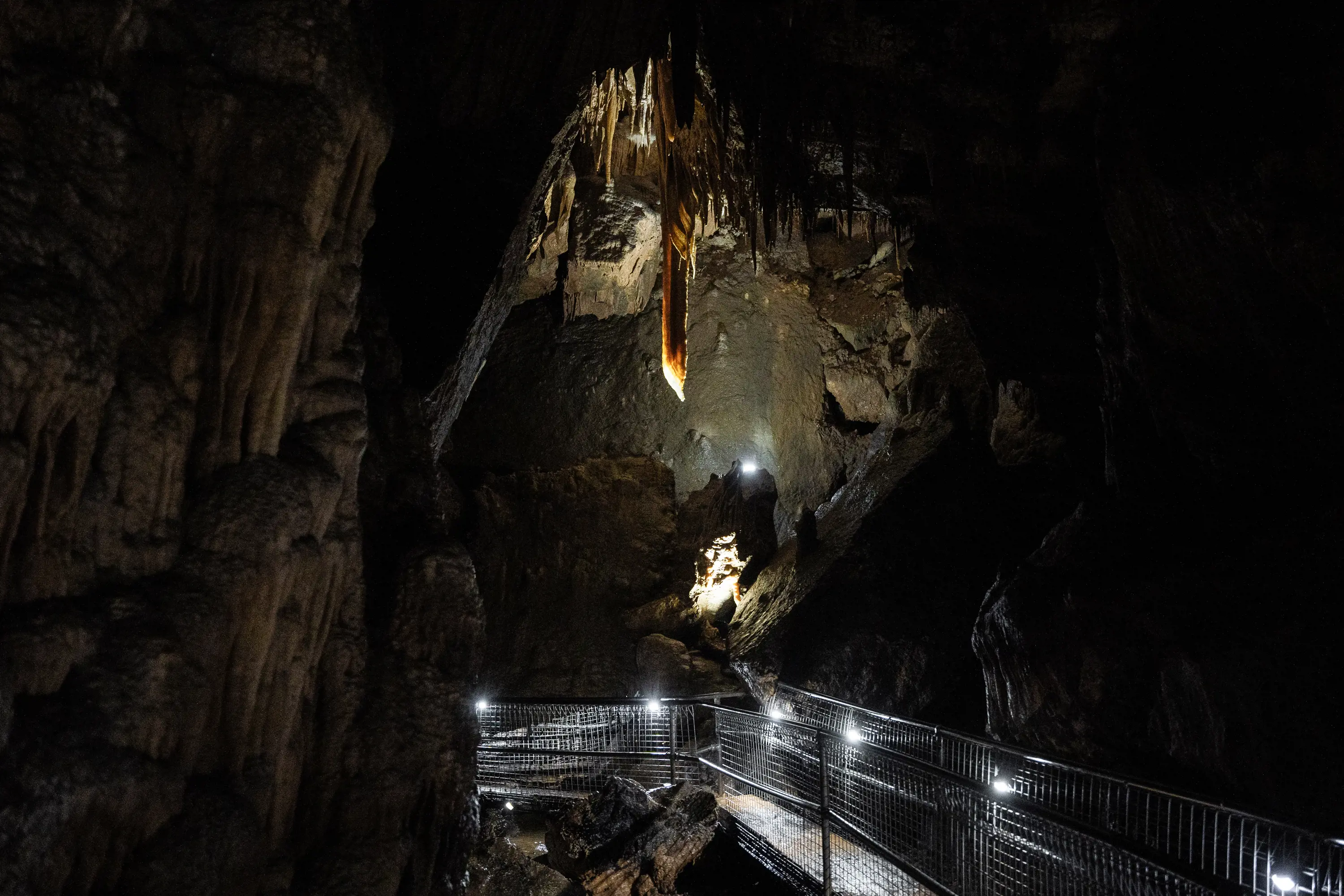 A large cave with a a metal walkway below a stalactite hanging from the cave ceiling.
