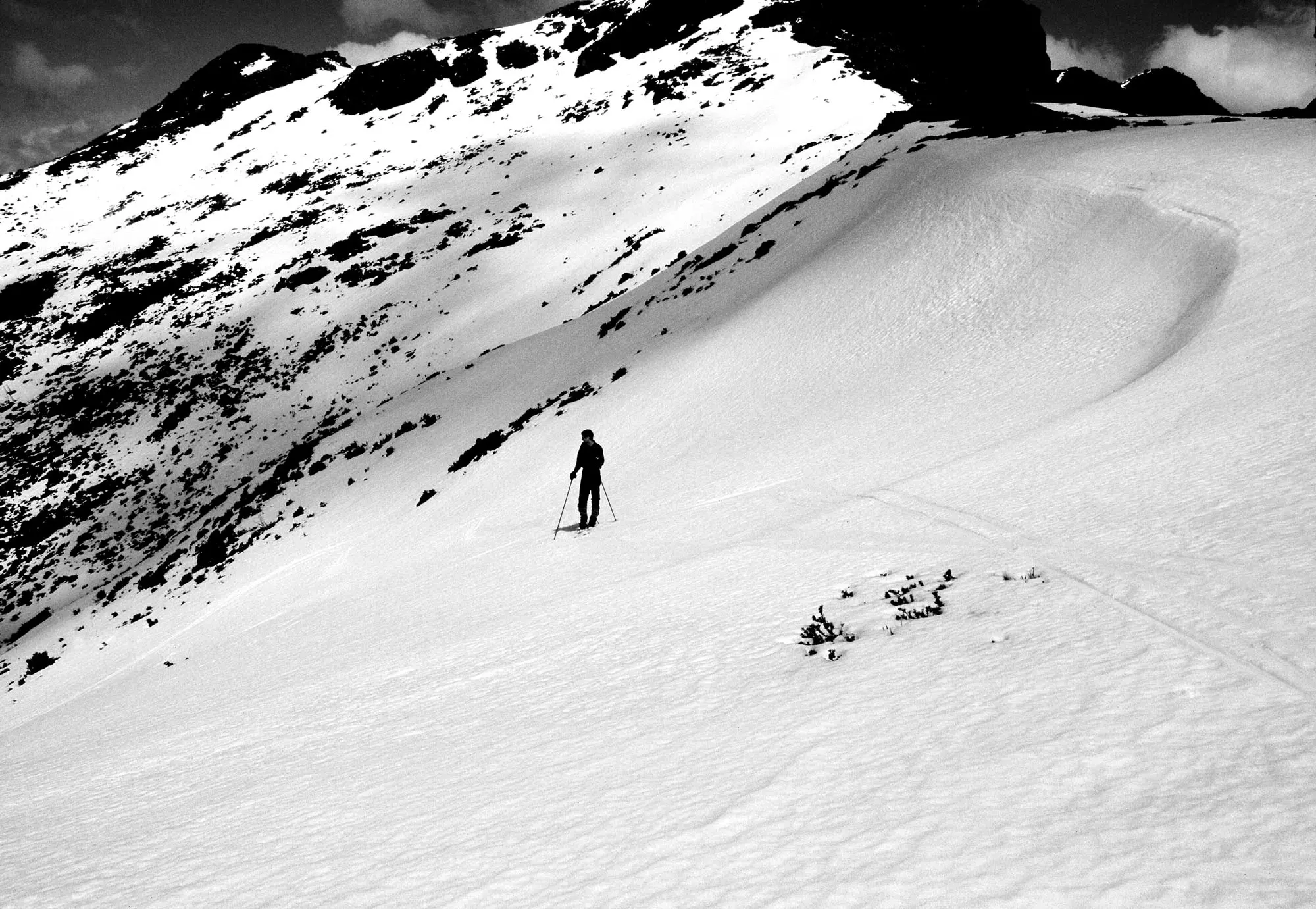 A man wearing skis stands on a gentle snow-covered slope.