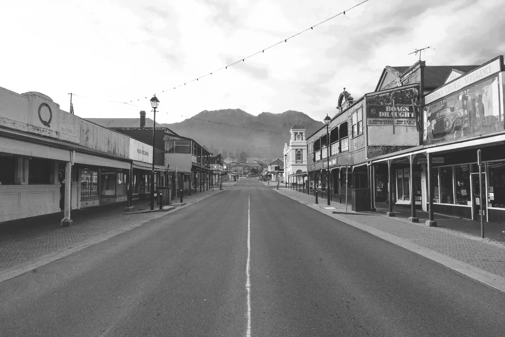 A black and white photo of a long, straight, wide main road through a small town. The symmetry of the buildings either side frame the mountain rising up in the background.