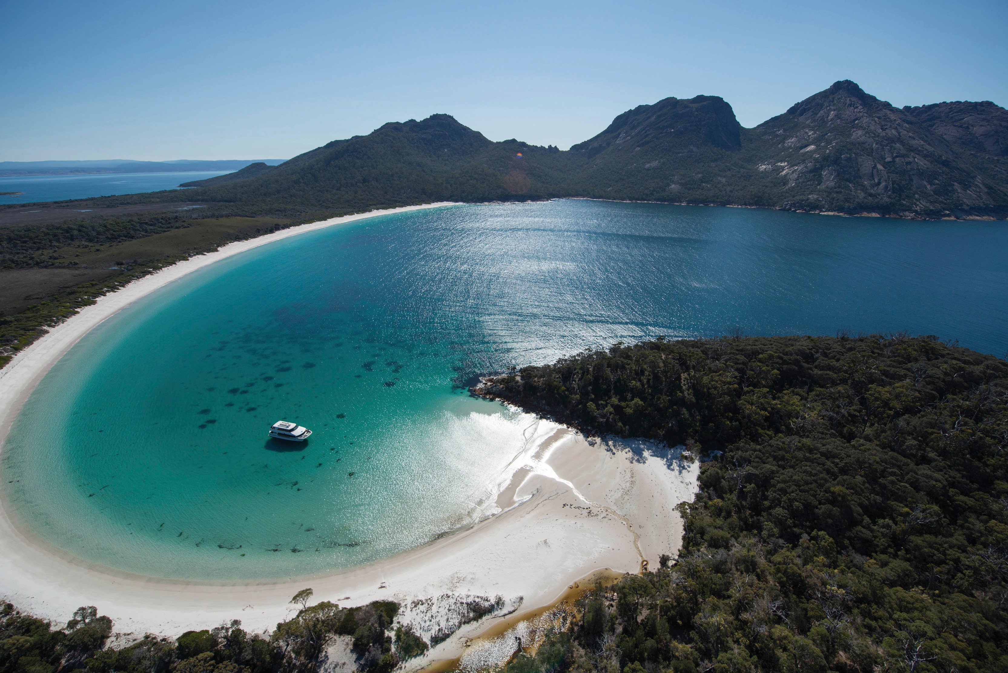 Stunning aerial image of Wineglass Bay on a clear, sunny day with crystal clear, blue water. Wineglass Bay Cruise boat is docked within the Bay.