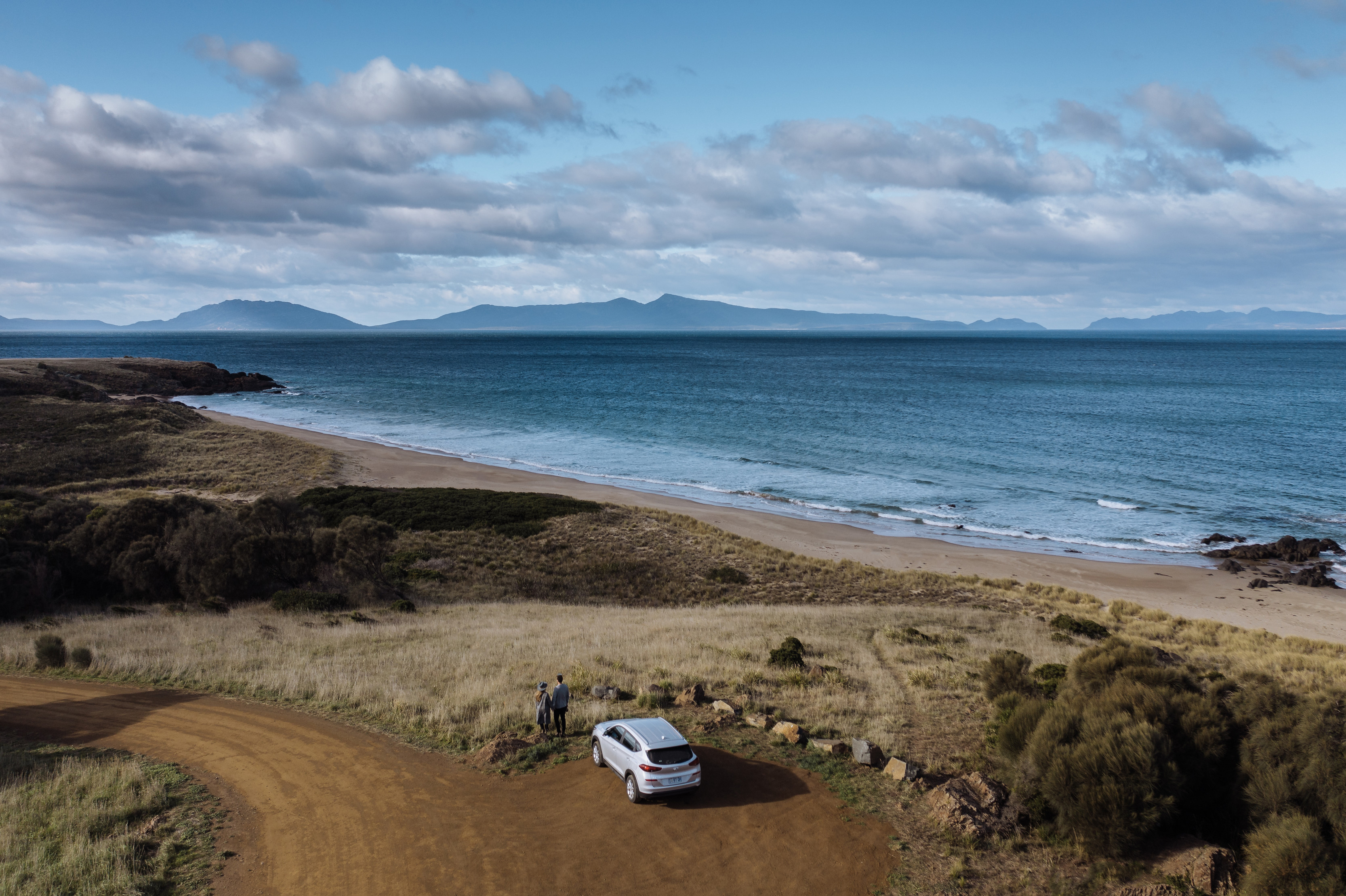 A couple on a road trip park their car at look at the ocean views whilst touring in Swansea.