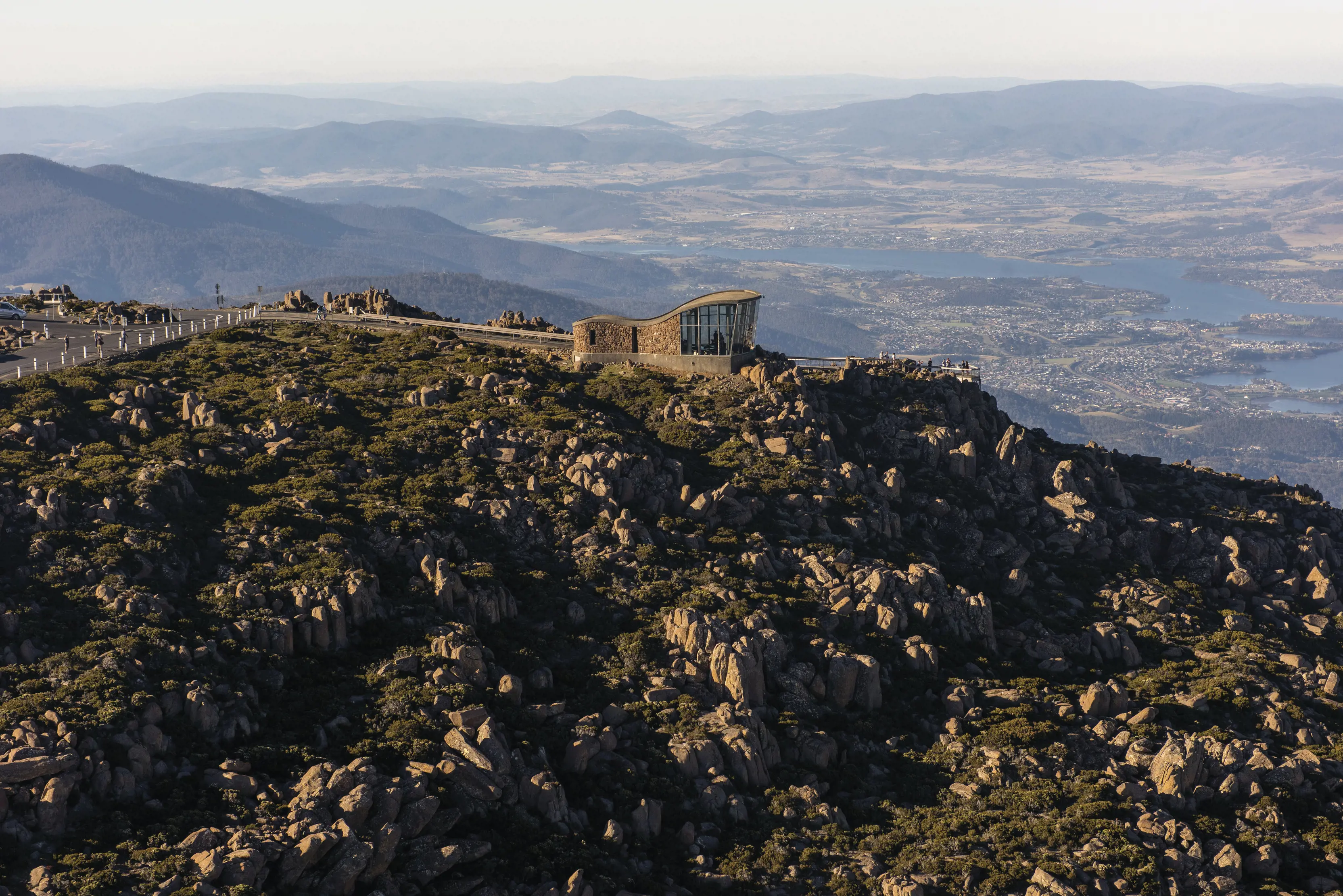 Incredible aerial view of Mt Wellington/ kunanyi with a lookout building at the top. Sun hits the rocks for a dramatic and vibrant scene.